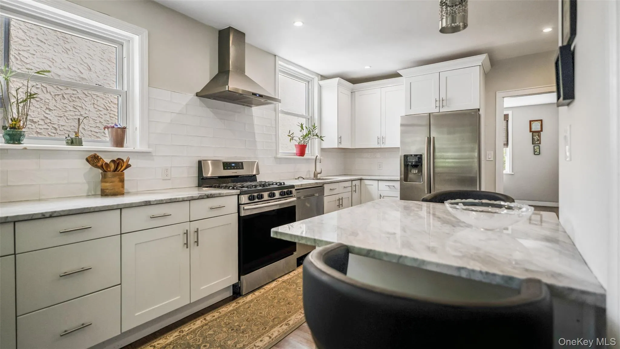 Modern kitchen featuring white shaker cabinetry, stainless steel appliances, a subway tile backsplash, and stone countertops Modern kitchen featuring white shaker cabinetry, stainless steel appliances, a subway tile backsplash, and stone countertops