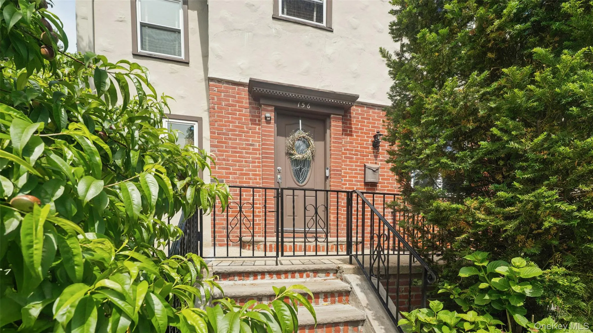 Brick and stucco facade featuring a prominent entry with a brown door, sidelights, and a decorative wreath Brick and stucco facade featuring a prominent entry with a brown door, sidelights, and a decorative wreath
