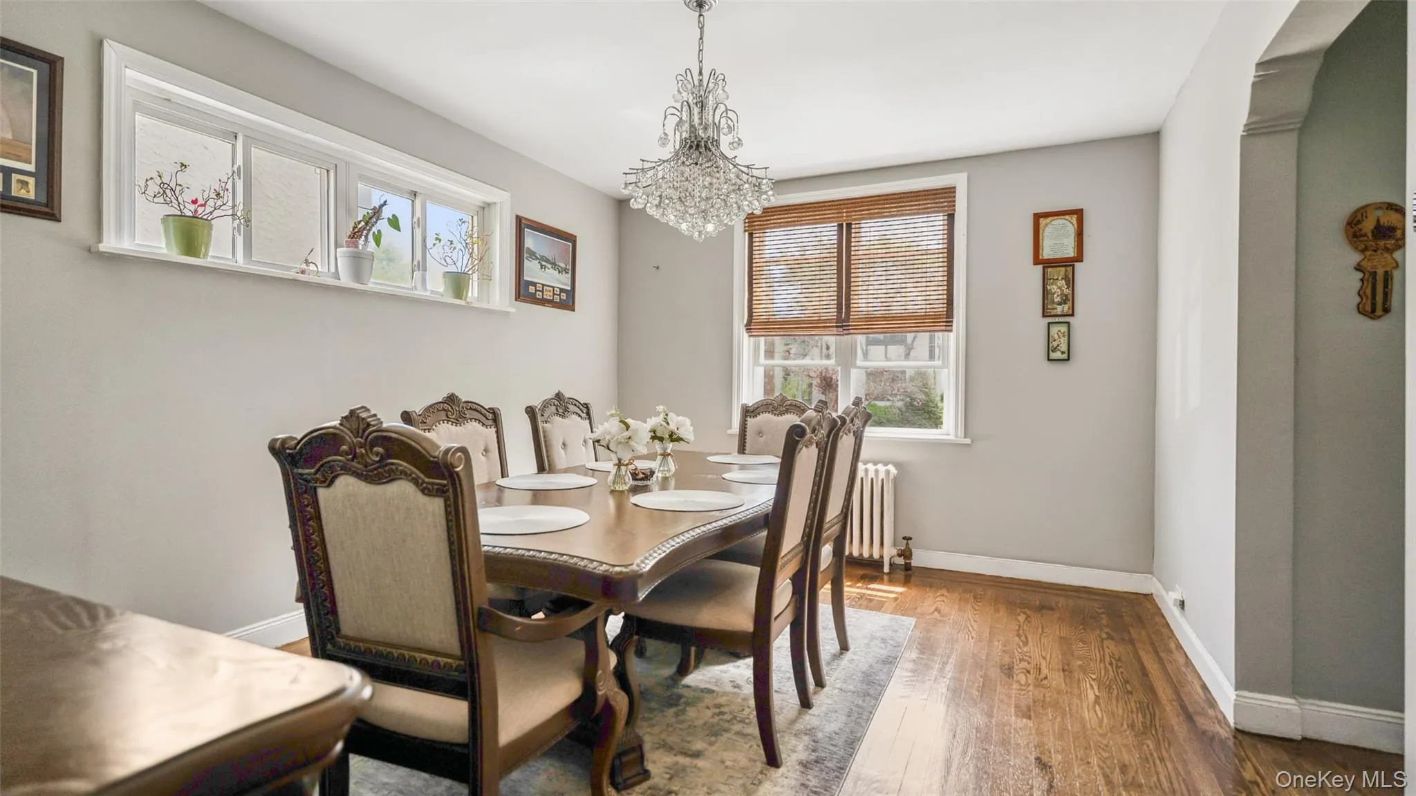 Dining area featuring hardwood flooring, light gray wall paint, a crystal chandelier, and two windows providing natural light Dining area featuring hardwood flooring, light gray wall paint, a crystal chandelier, and two windows providing natural light