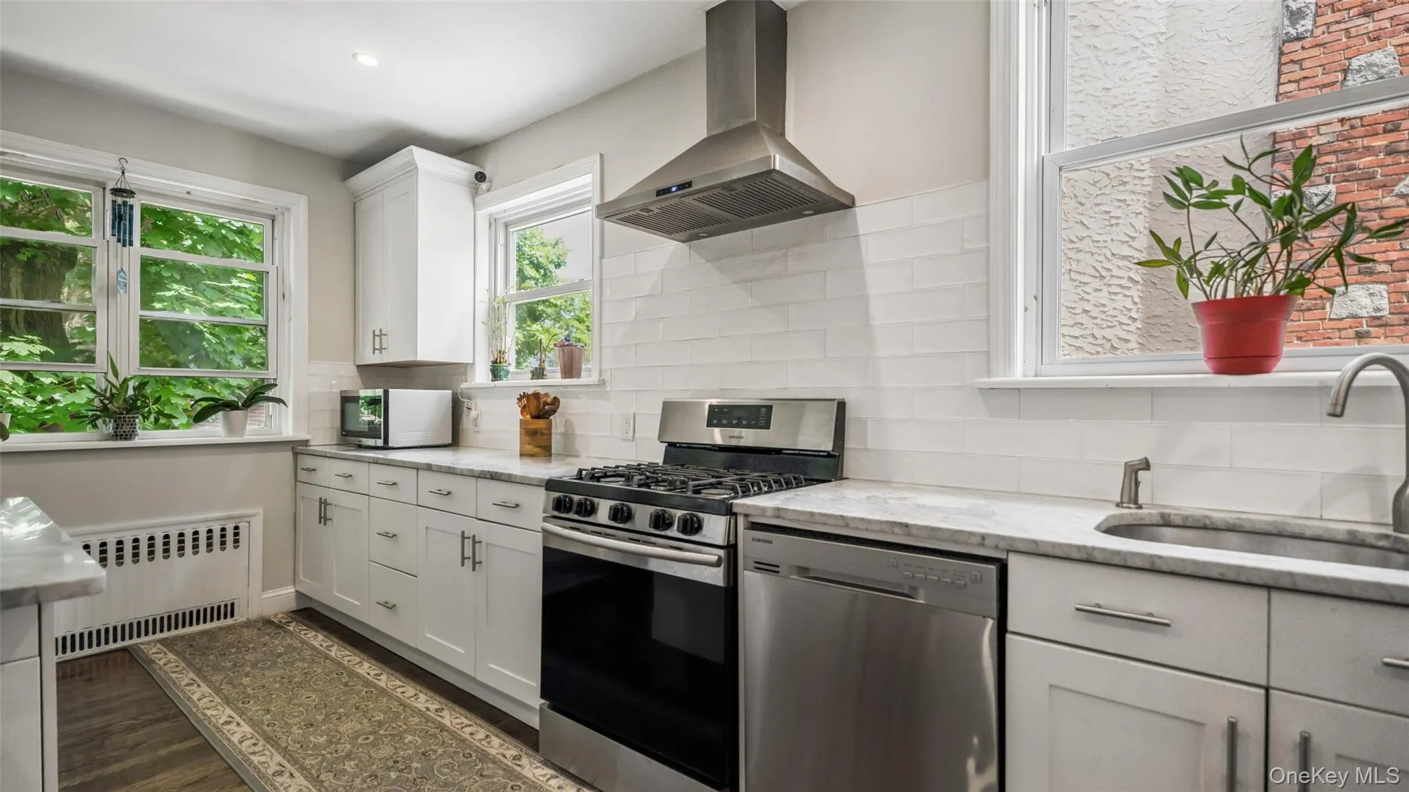Kitchen featuring white shaker-style cabinetry, stainless steel appliances, a stainless steel range hood, white subway tile backsplash, and light-toned countertops Kitchen featuring white shaker-style cabinetry, stainless steel appliances, a stainless steel range hood, white subway tile backsplash, and light-toned countertops