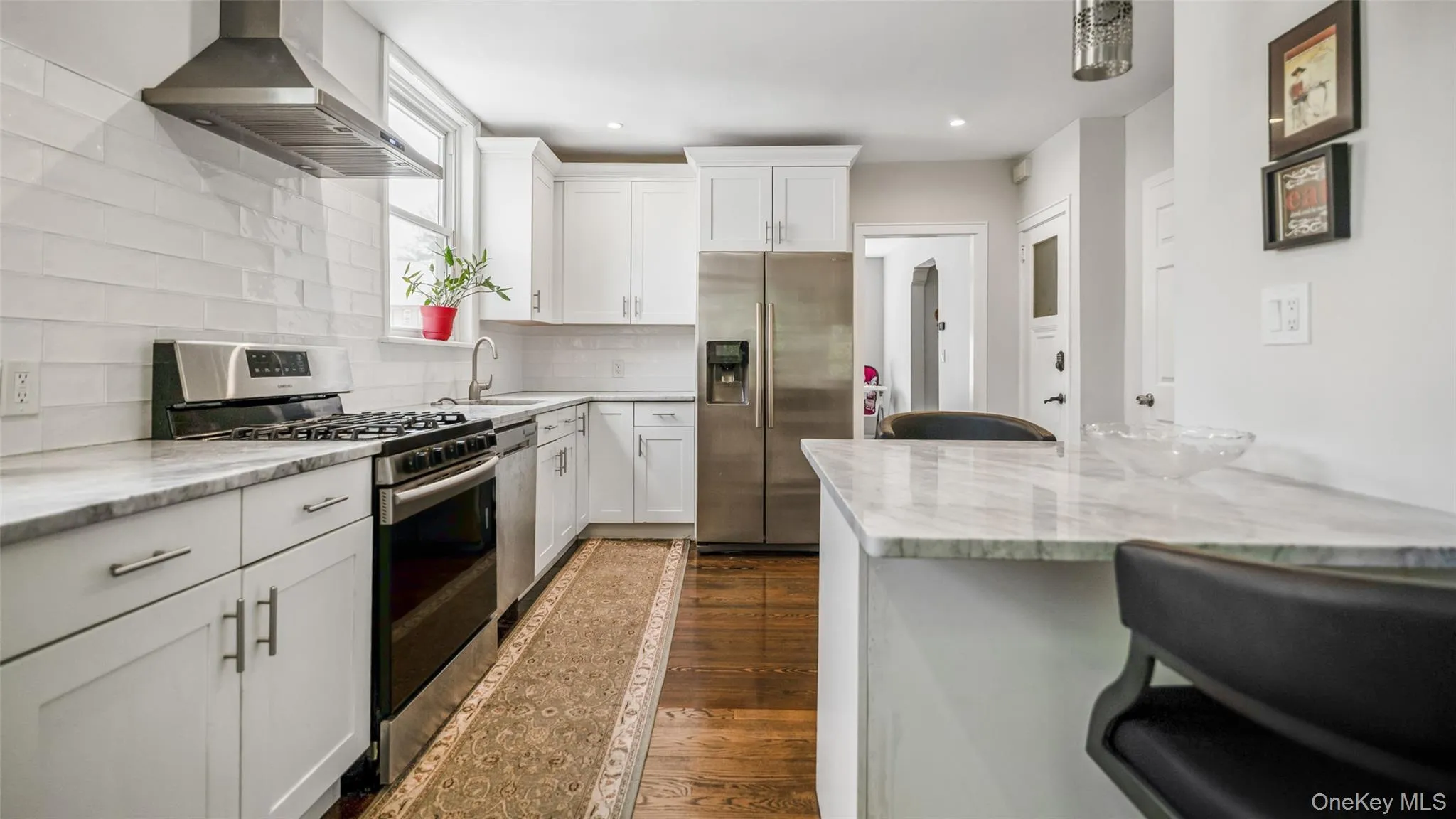 Modern kitchen featuring white shaker cabinetry, stainless steel appliances, a gas range with a coordinating hood, stone countertops, and a subway tile backsplash Modern kitchen featuring white shaker cabinetry, stainless steel appliances, a gas range with a coordinating hood, stone countertops, and a subway tile backsplash