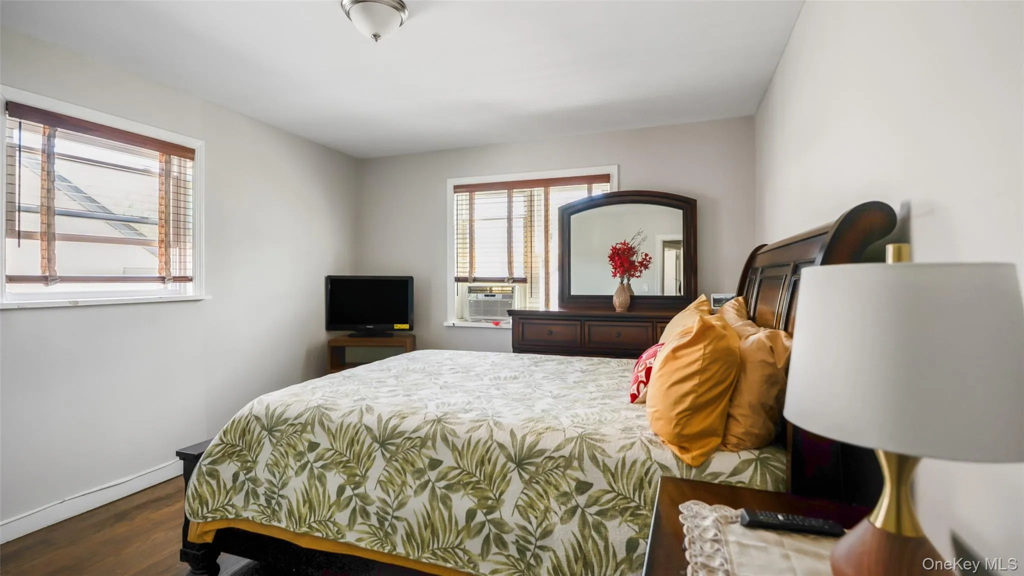 Bedroom featuring two windows with wood blinds, wood-finish flooring, and a ceiling-mounted light fixture Bedroom featuring two windows with wood blinds, wood-finish flooring, and a ceiling-mounted light fixture