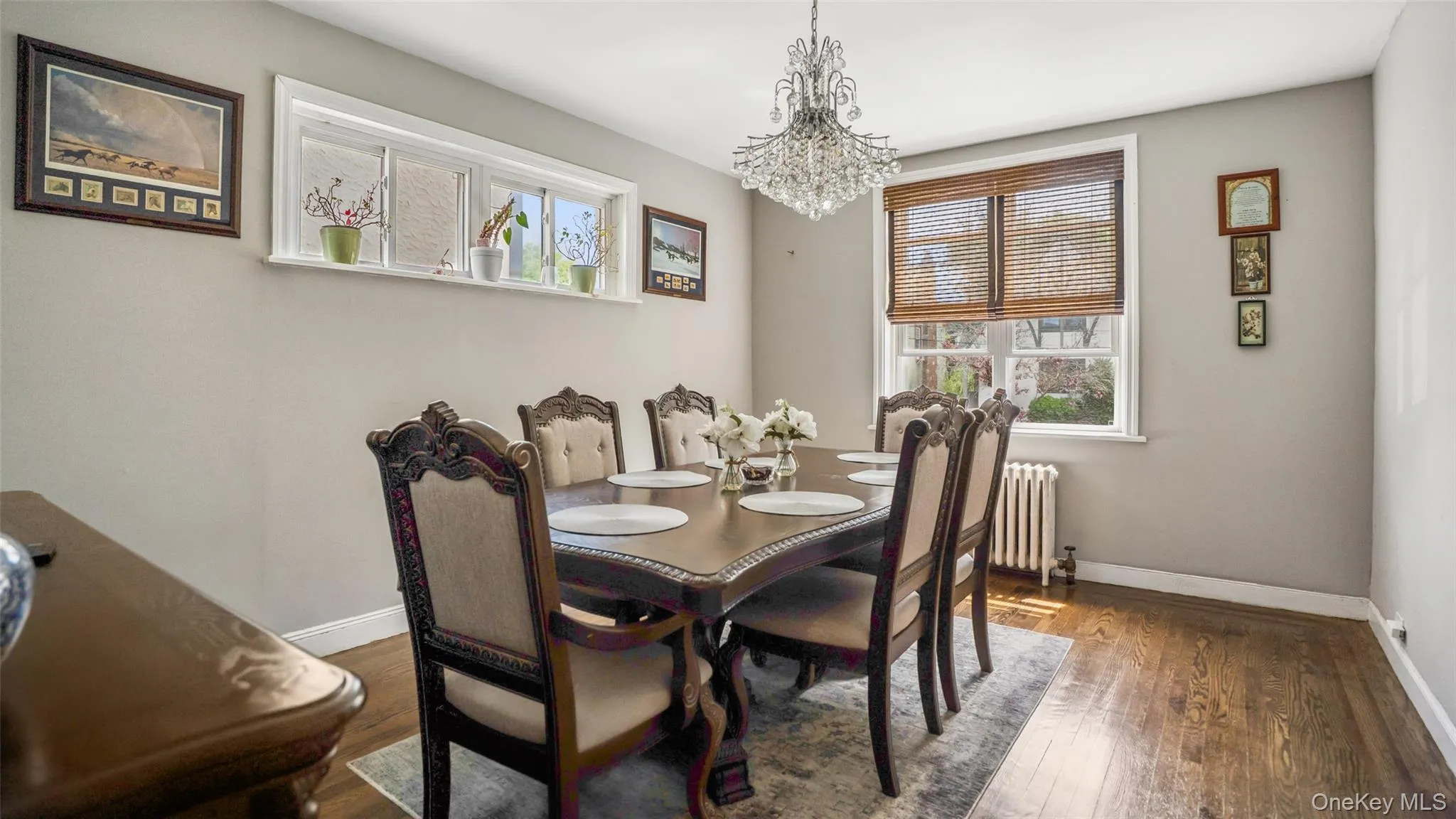 Dining area featuring a crystal chandelier, wood-finish flooring, a large window with natural light, and neutral wall tones Dining area featuring a crystal chandelier, wood-finish flooring, a large window with natural light, and neutral wall tones