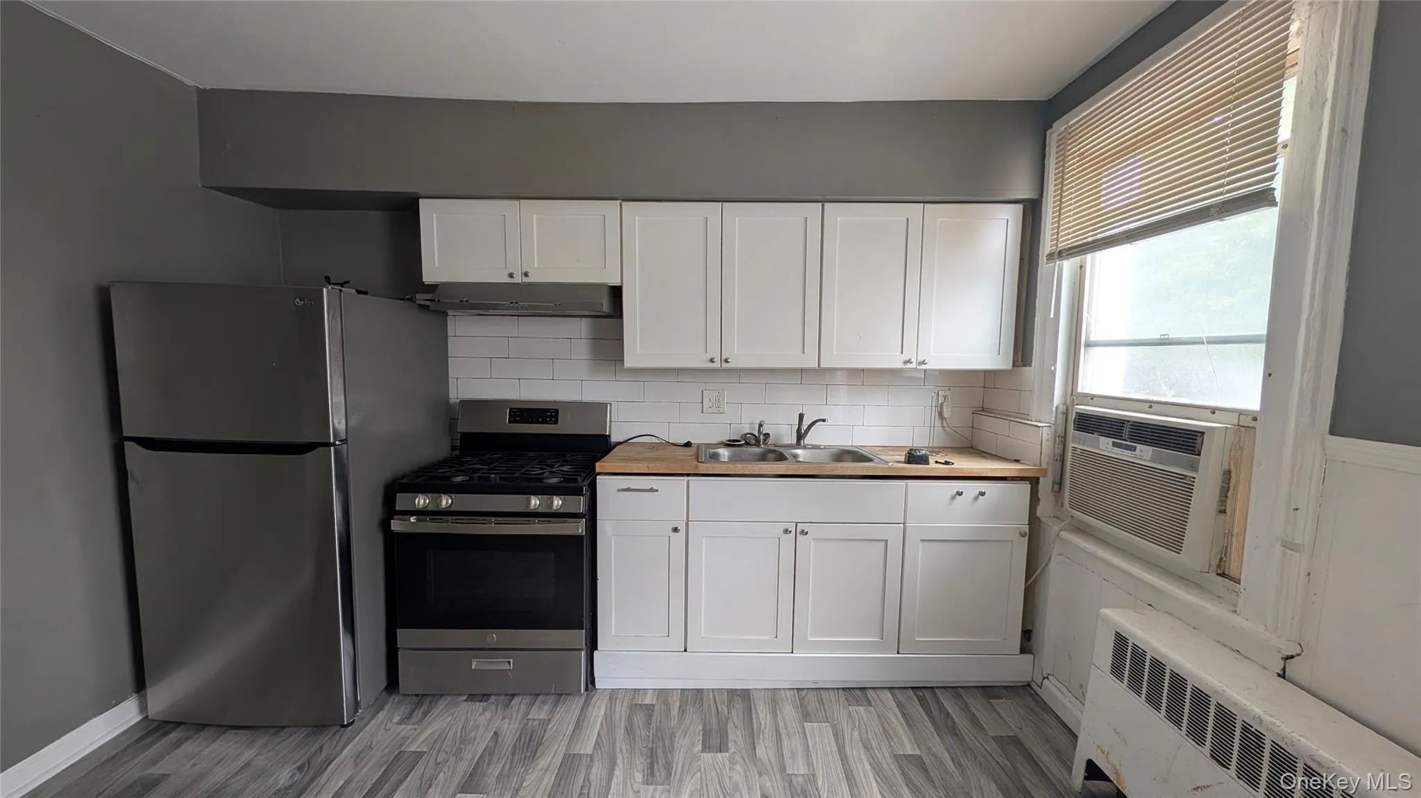 Kitchen featuring white cabinetry, wood-finish countertops, subway tile backsplash, stainless steel appliances, and wood-look flooring Kitchen featuring white cabinetry, wood-finish countertops, subway tile backsplash, stainless steel appliances, and wood-look flooring
