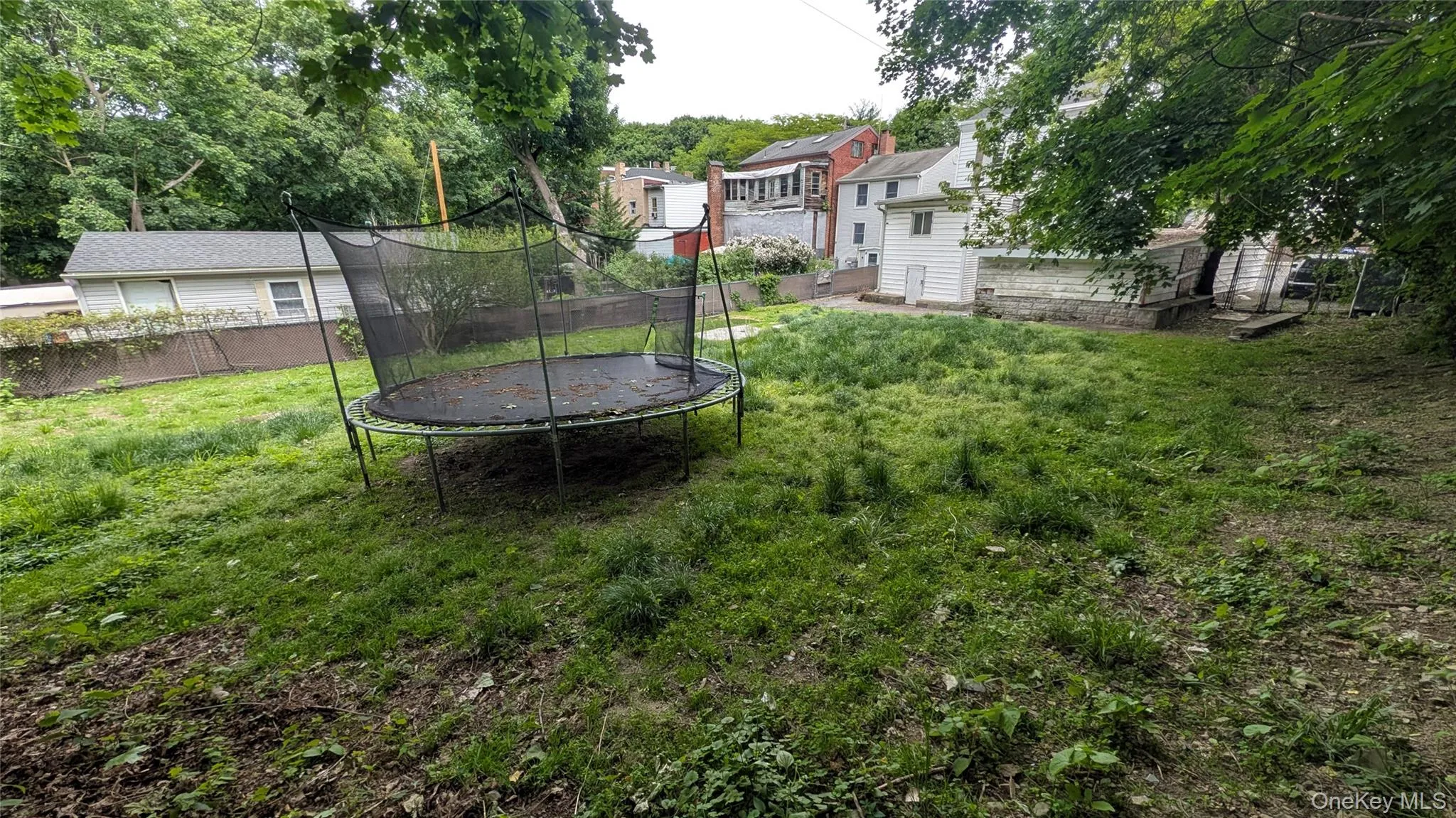 Spacious, sloped backyard featuring abundant natural greenery and a built-in trampoline Spacious, sloped backyard featuring abundant natural greenery and a built-in trampoline