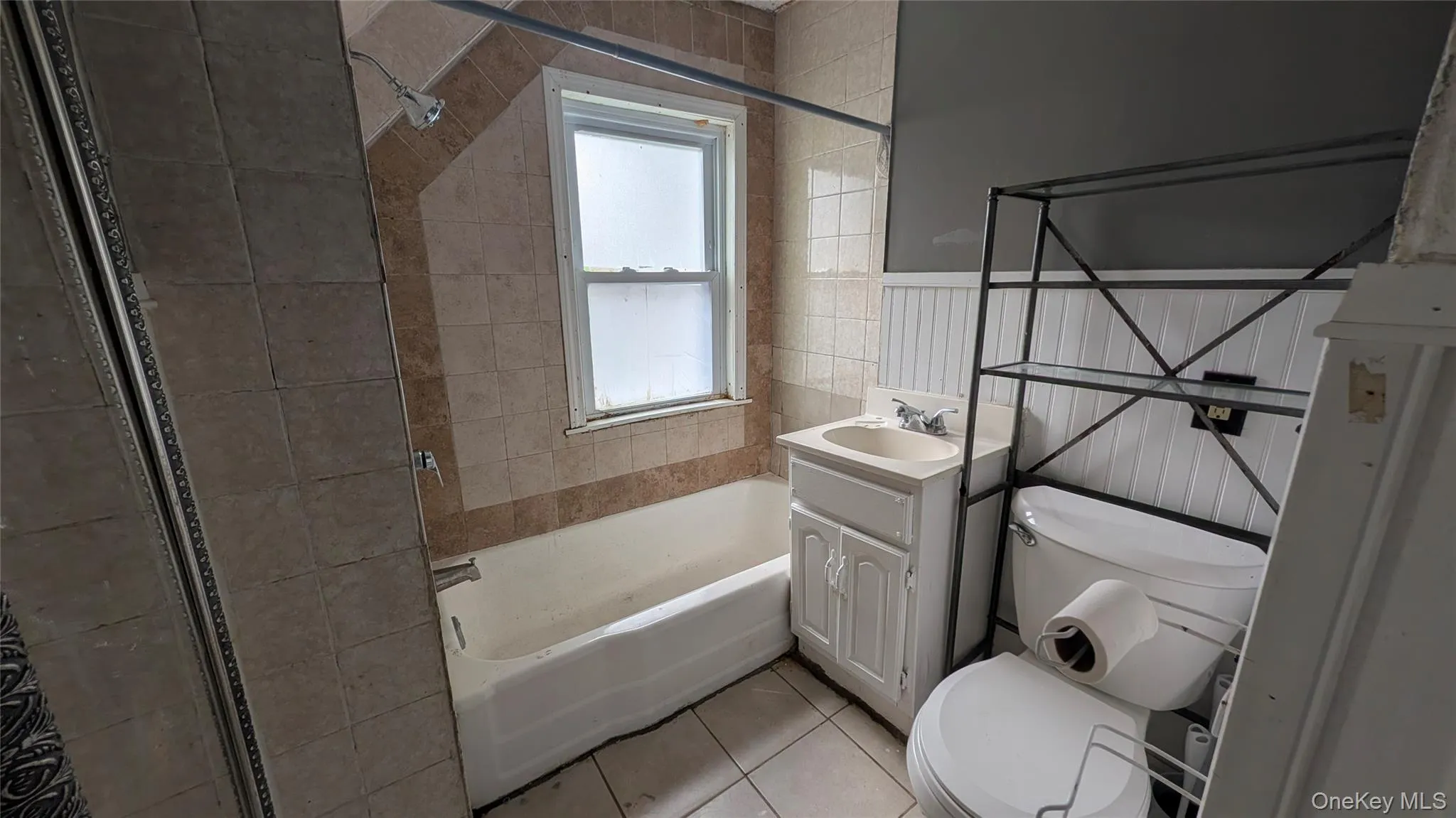 Bathroom featuring a white bathtub, ceramic tile surround, and a window with frosted privacy glass Bathroom featuring a white bathtub, ceramic tile surround, and a window with frosted privacy glass