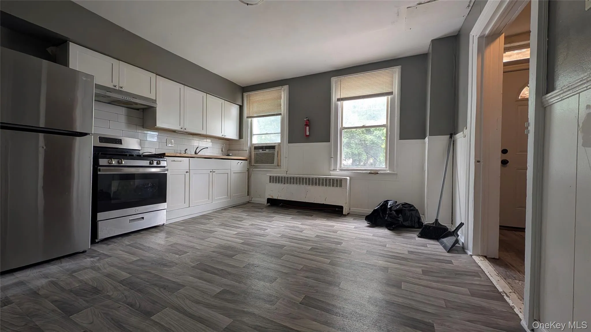 Kitchen featuring white cabinetry, stainless steel appliances, a white subway tile backsplash, and wood-finish flooring Kitchen featuring white cabinetry, stainless steel appliances, a white subway tile backsplash, and wood-finish flooring