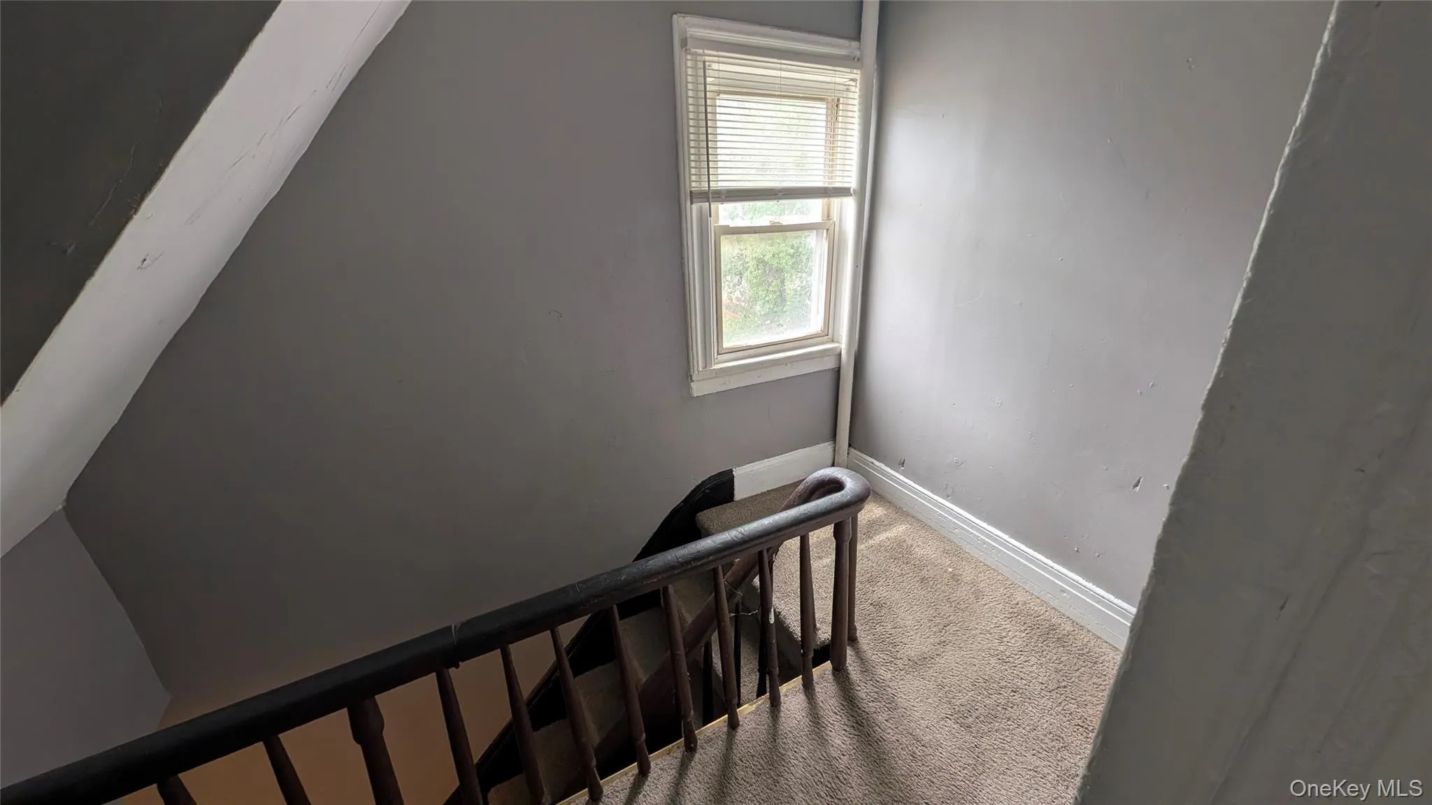 Carpeted landing featuring a window with blinds, dark wood banister, and grey painted walls Carpeted landing featuring a window with blinds, dark wood banister, and grey painted walls