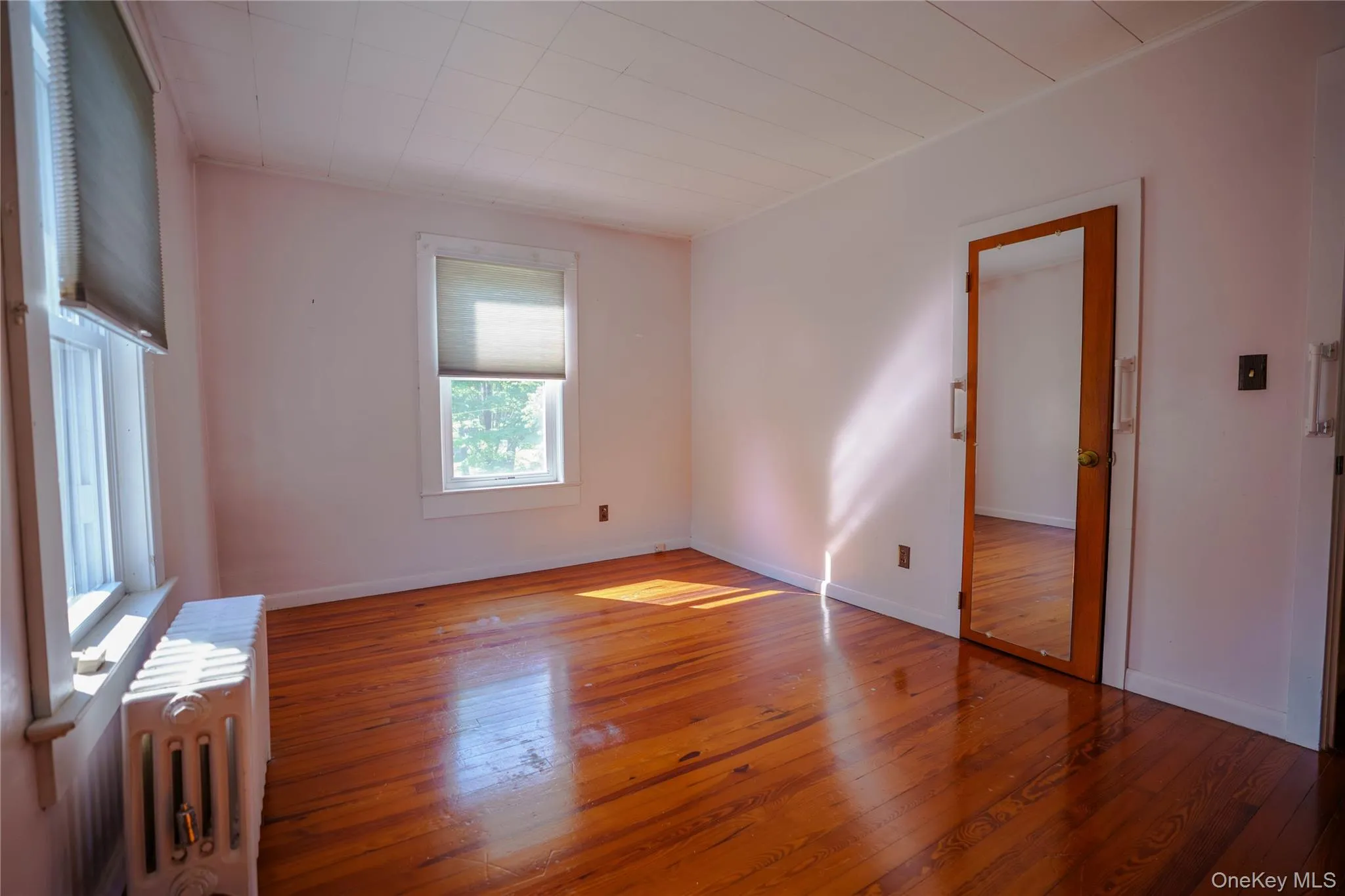 Spacious room featuring wood-finish flooring, white walls, and a white ceiling Spacious room featuring wood-finish flooring, white walls, and a white ceiling