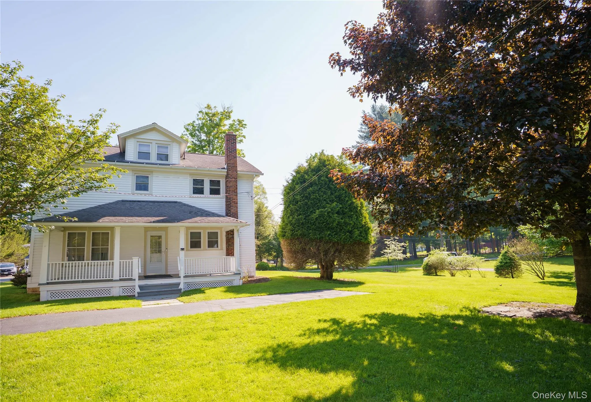 White two-story residence featuring a covered front porch with white railings, multiple windows, and a prominent brick chimney White two-story residence featuring a covered front porch with white railings, multiple windows, and a prominent brick chimney