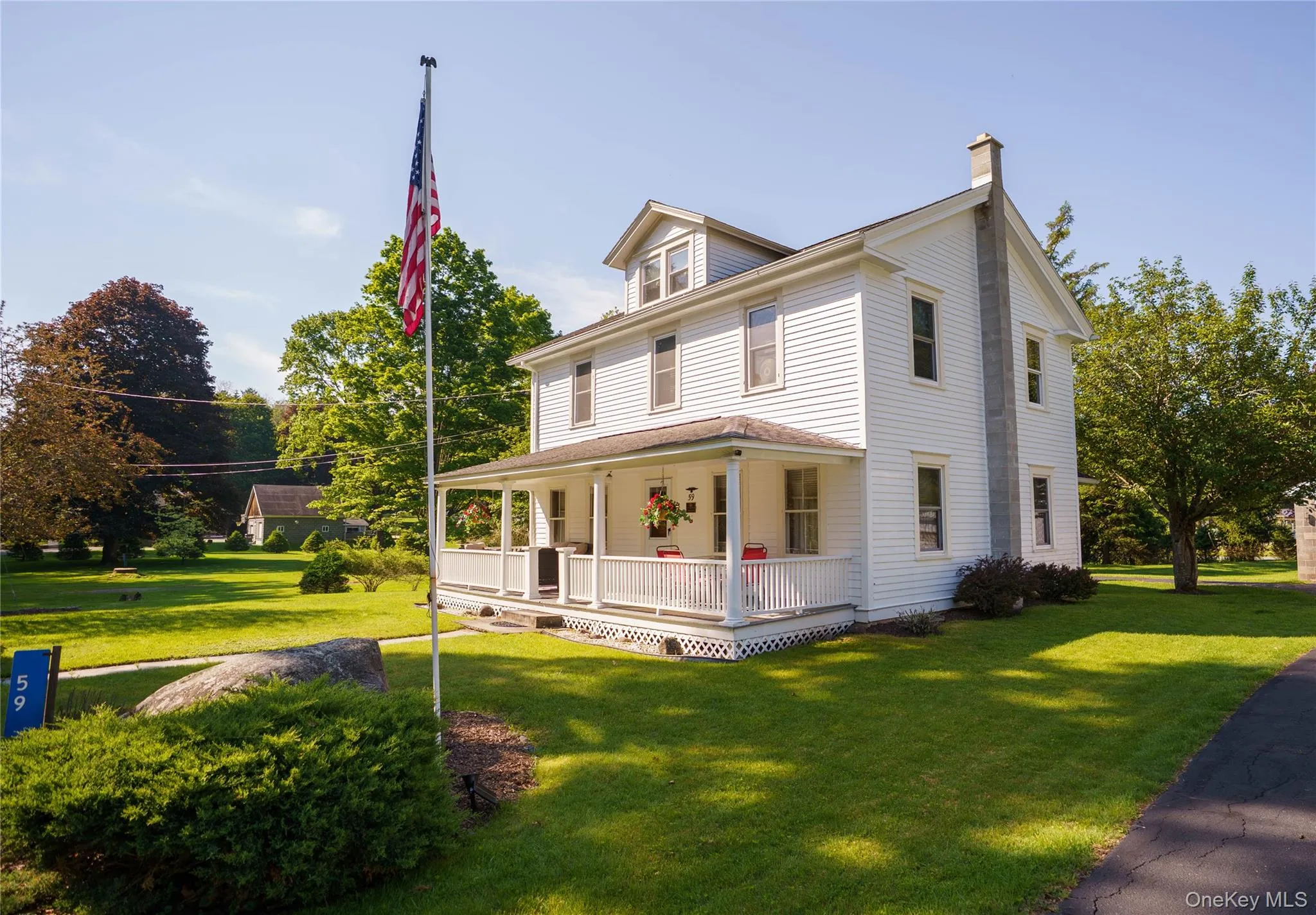 Two-story white residence featuring a full-width front porch with white railings, a prominent side chimney, and a dormer window Two-story white residence featuring a full-width front porch with white railings, a prominent side chimney, and a dormer window
