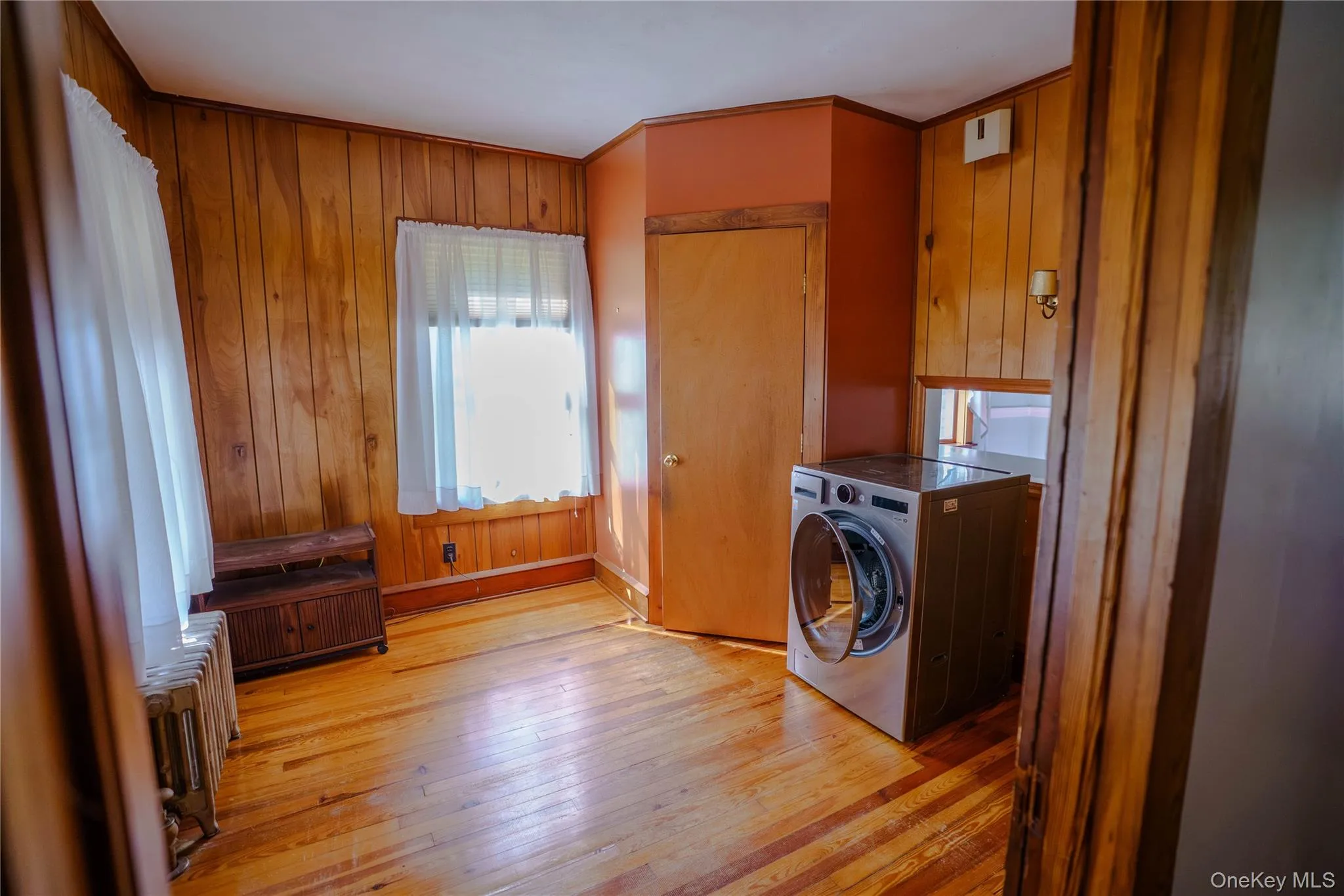 Room featuring wood-paneled walls, hardwood flooring, and a window with natural light Room featuring wood-paneled walls, hardwood flooring, and a window with natural light