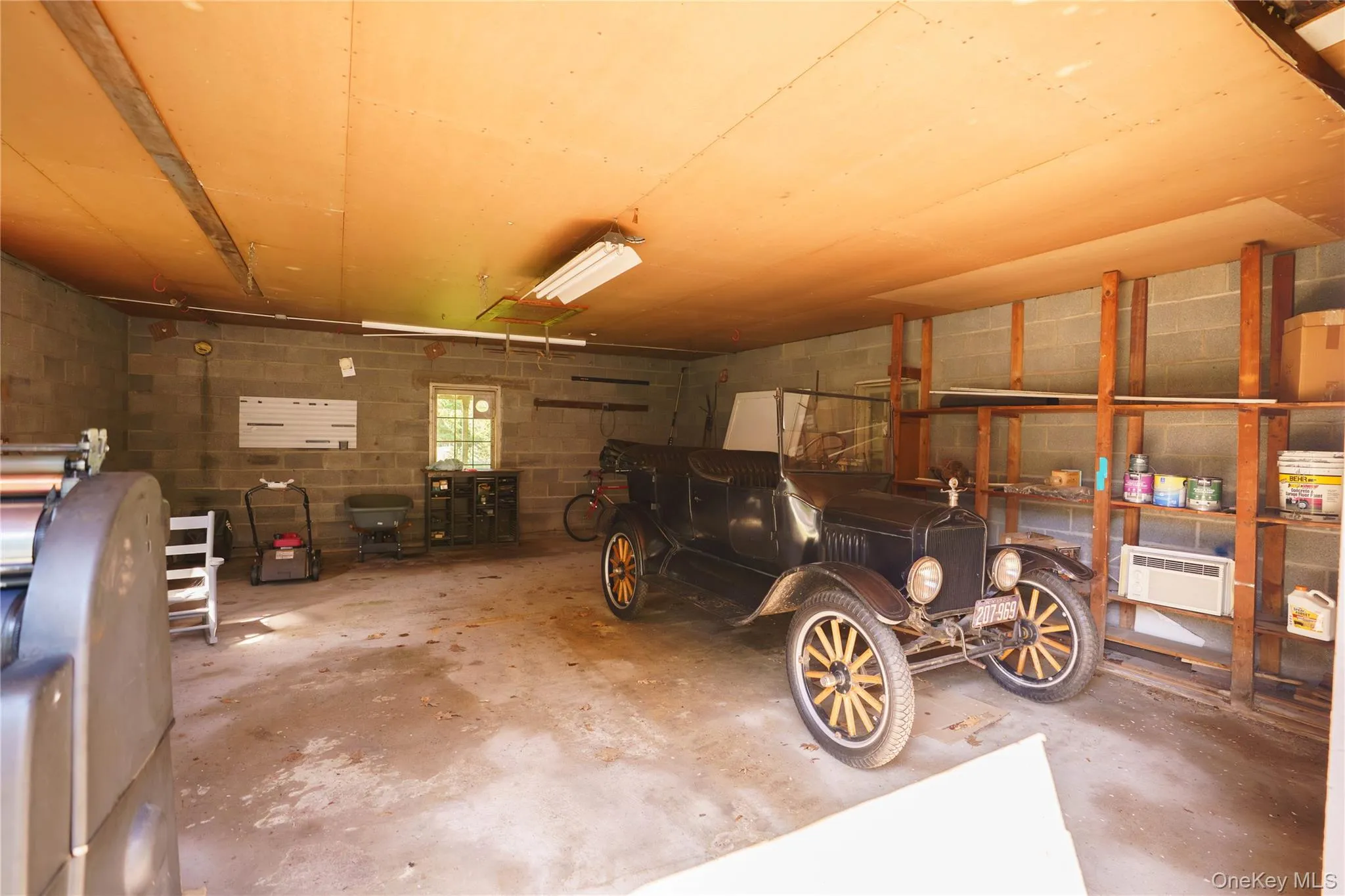 Spacious garage featuring concrete block walls, a concrete floor, built-in shelving, and a single window for natural light Spacious garage featuring concrete block walls, a concrete floor, built-in shelving, and a single window for natural light