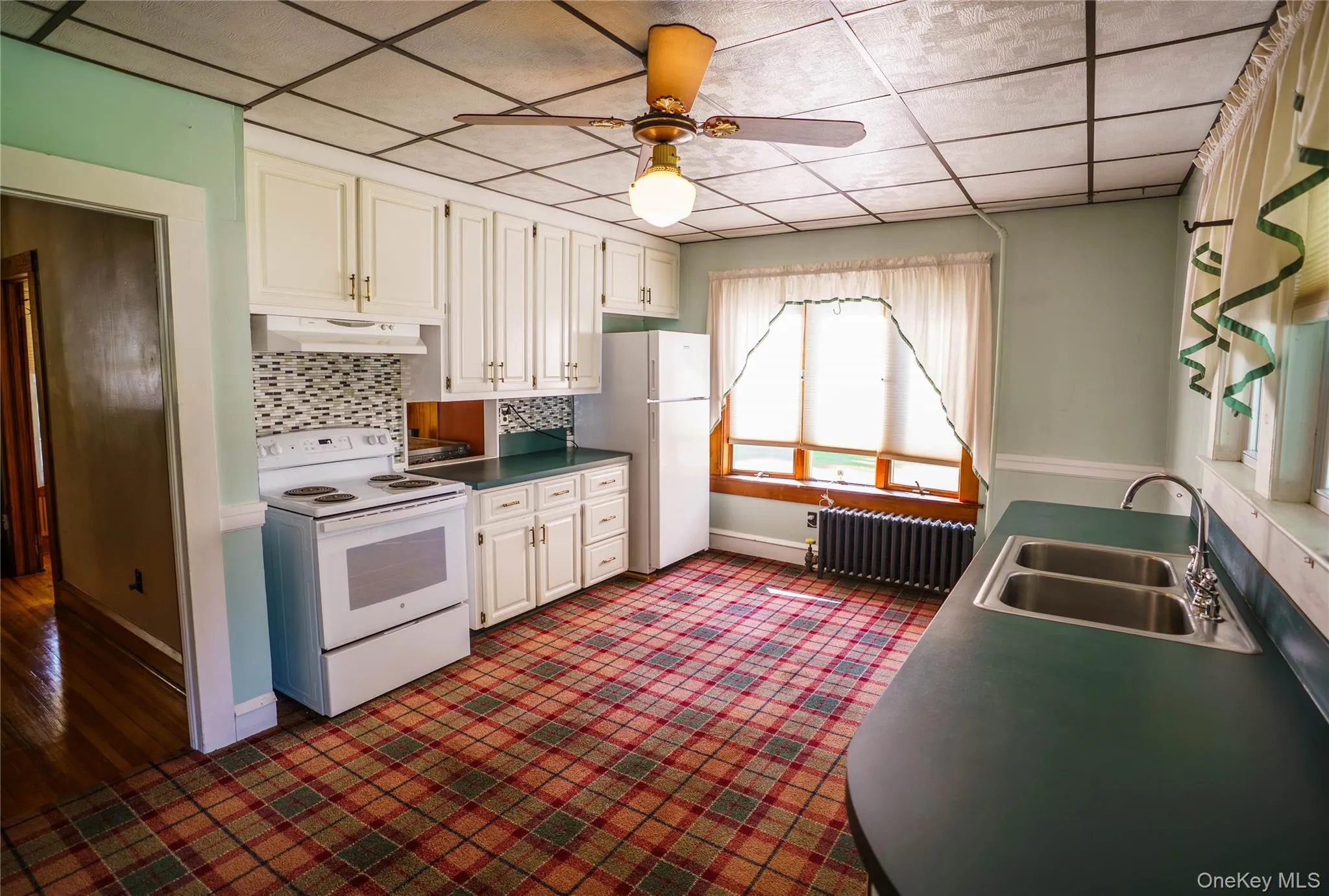 Kitchen featuring ample white cabinetry, a dual-basin sink, and a tiled backsplash Kitchen featuring ample white cabinetry, a dual-basin sink, and a tiled backsplash