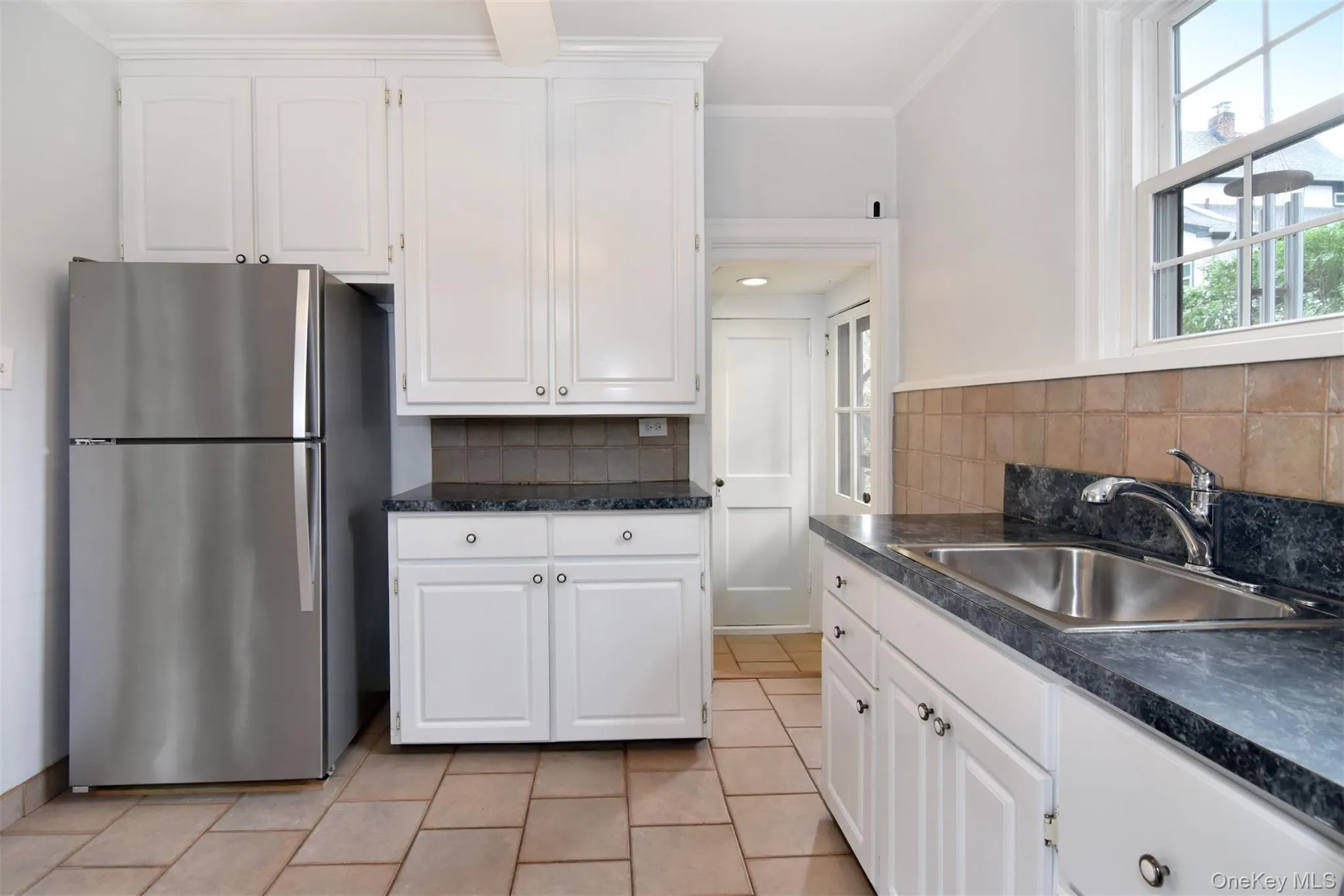 Kitchen featuring white cabinetry, dark countertops, tiled backsplash, stainless steel appliances, and tile flooring Kitchen featuring white cabinetry, dark countertops, tiled backsplash, stainless steel appliances, and tile flooring