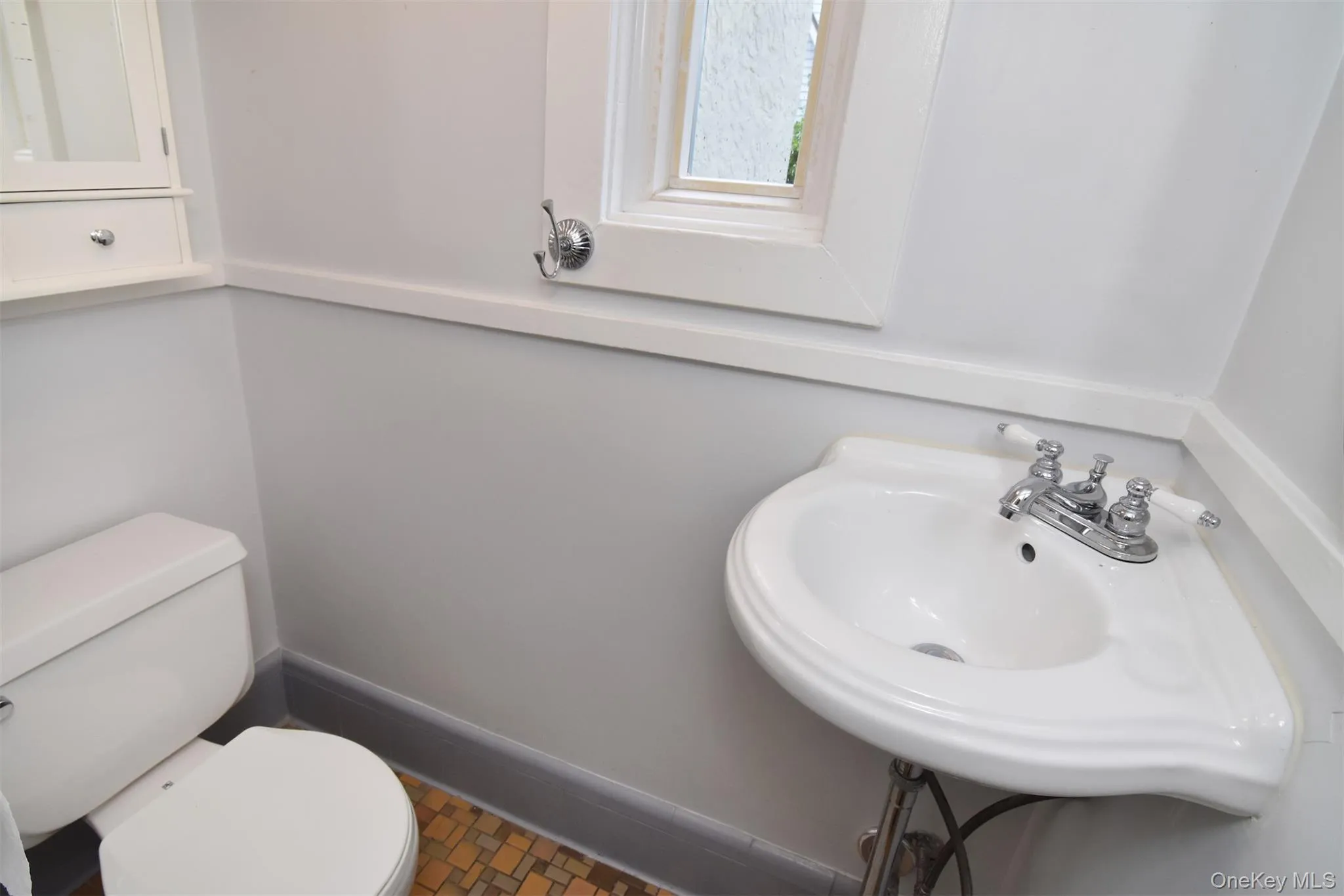 Powder room featuring a pedestal sink, white toilet, and a window with white trim Powder room featuring a pedestal sink, white toilet, and a window with white trim