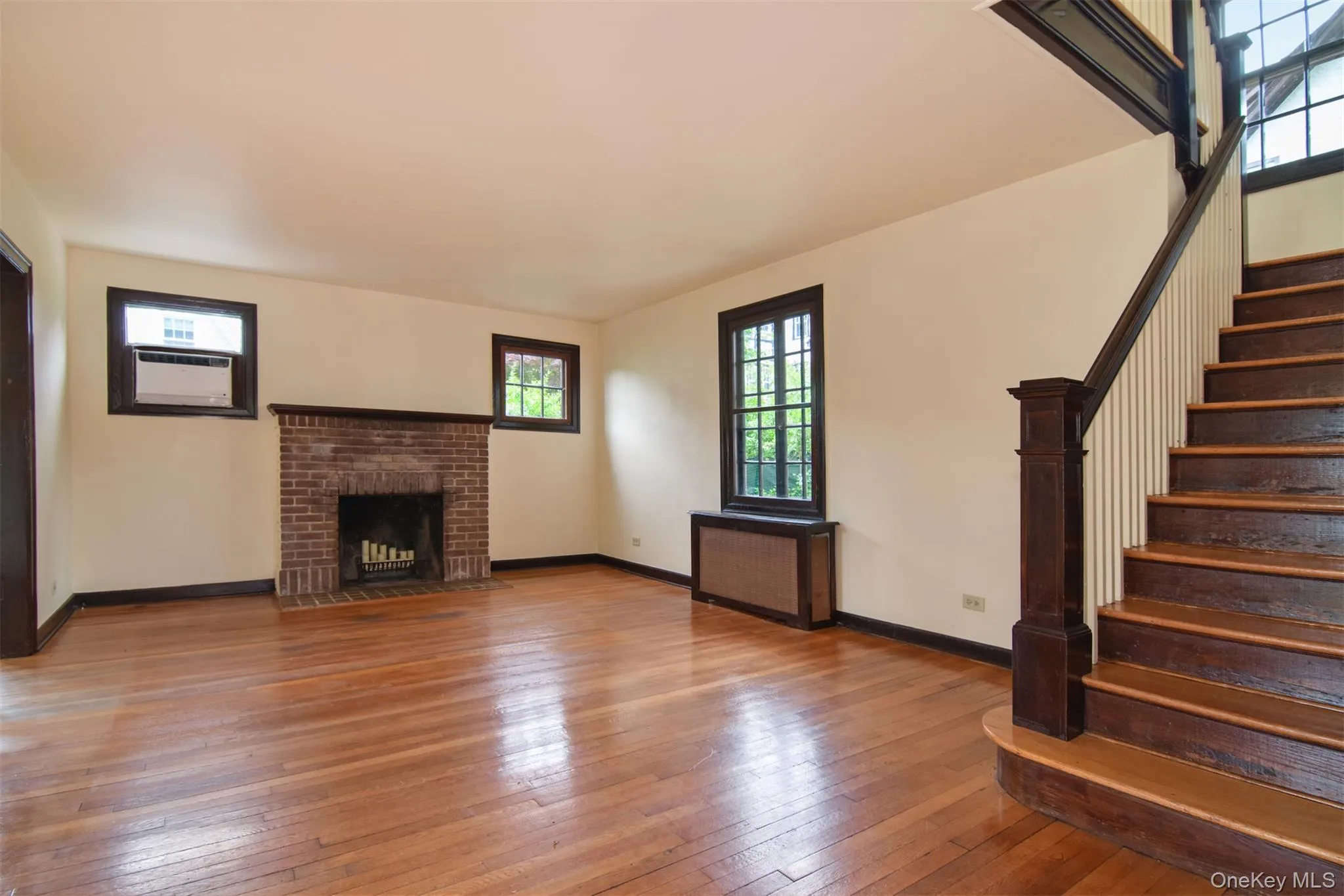 Spacious interior featuring wood-finish flooring and a brick fireplace Spacious interior featuring wood-finish flooring and a brick fireplace