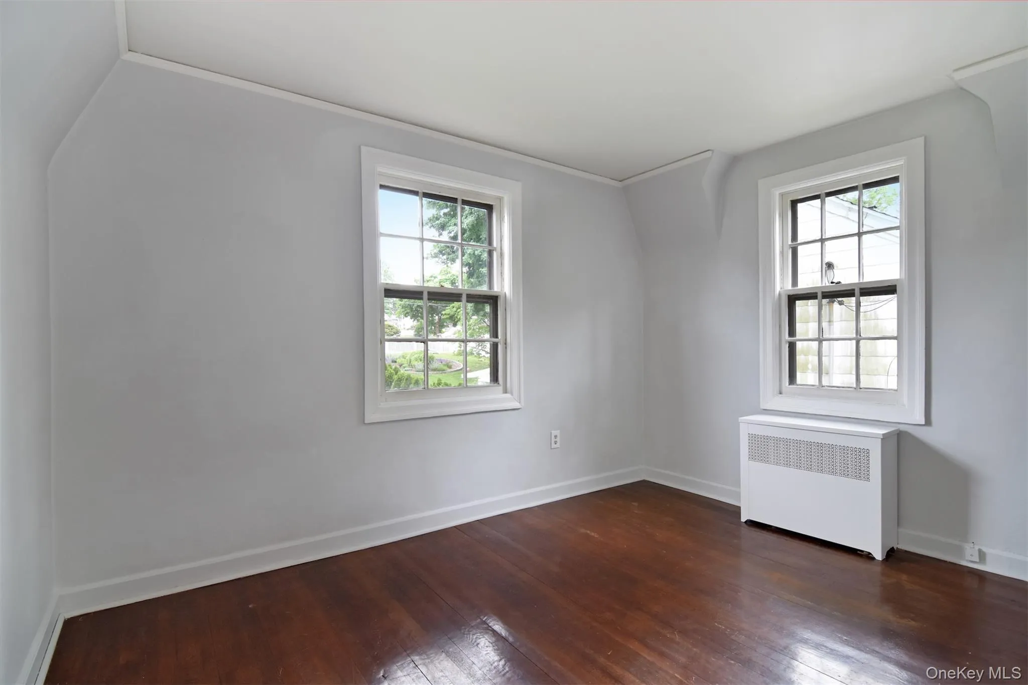 Bedroom featuring rich hardwood flooring, light gray wall paint, and white trim Bedroom featuring rich hardwood flooring, light gray wall paint, and white trim