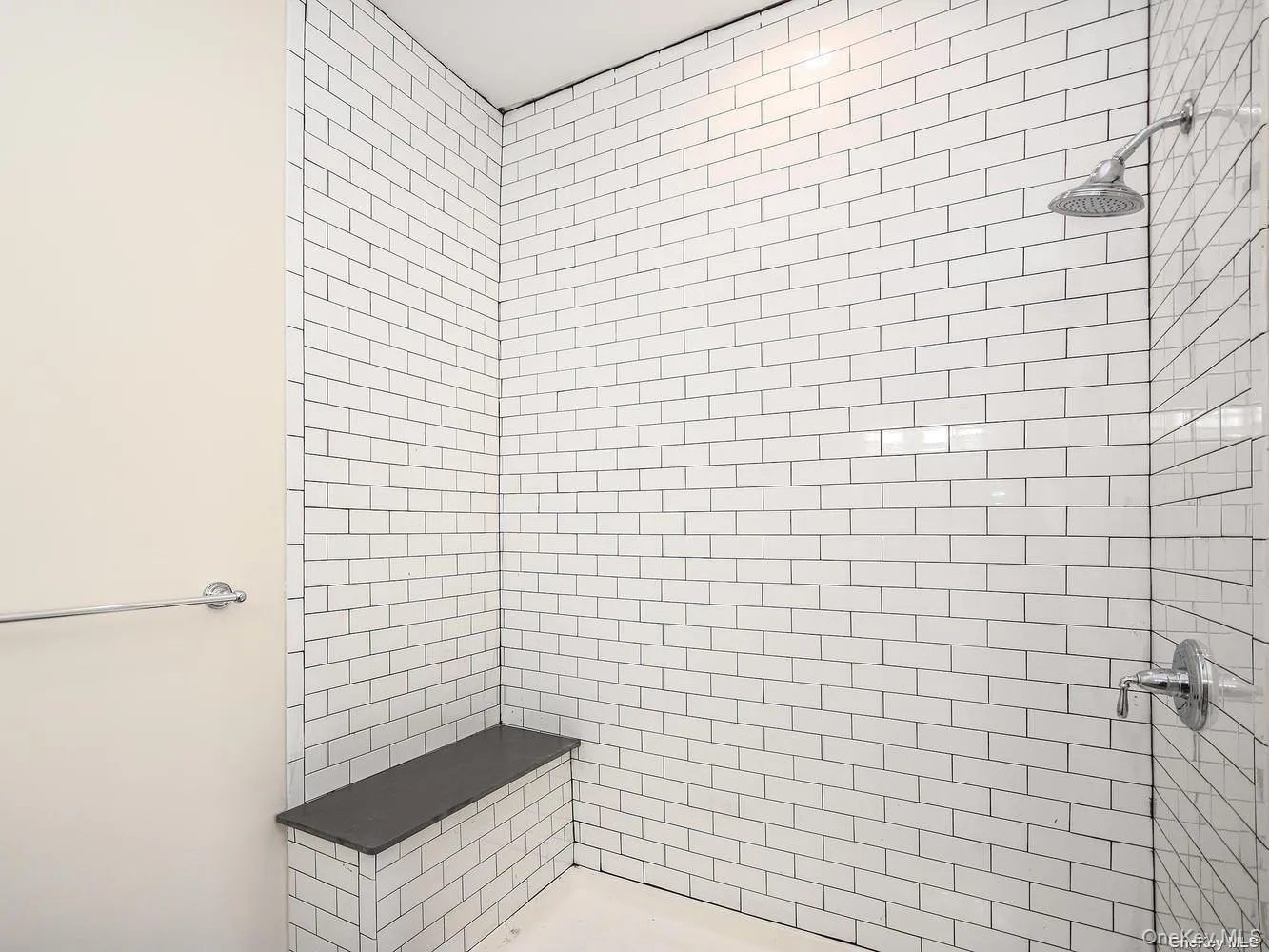 Shower enclosure featuring subway tile walls, a built-in bench with a dark countertop, and polished chrome fixtures Shower enclosure featuring subway tile walls, a built-in bench with a dark countertop, and polished chrome fixtures