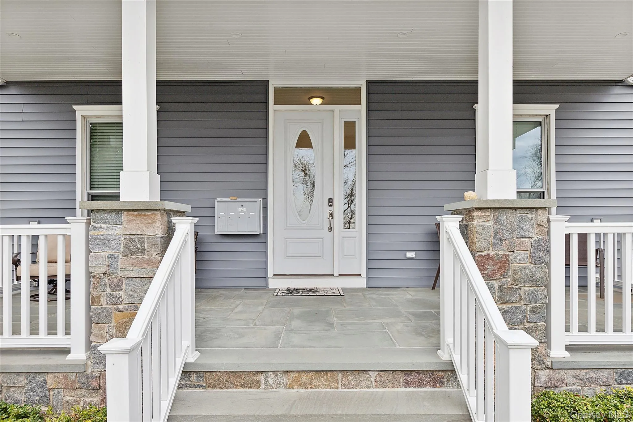 Covered front porch featuring stone-clad columns, white railings, and a slate-style entryway Covered front porch featuring stone-clad columns, white railings, and a slate-style entryway