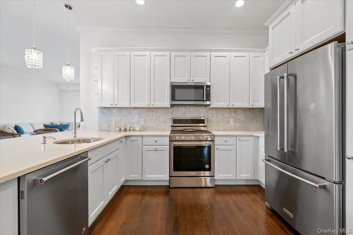 Kitchen with stainless steelappliances, white cabinetry,decorative light fixtures, darkwood-style floors, andornamental molding Kitchen with stainless steelappliances, white cabinetry,decorative light fixtures, darkwood-style floors, andornamental molding