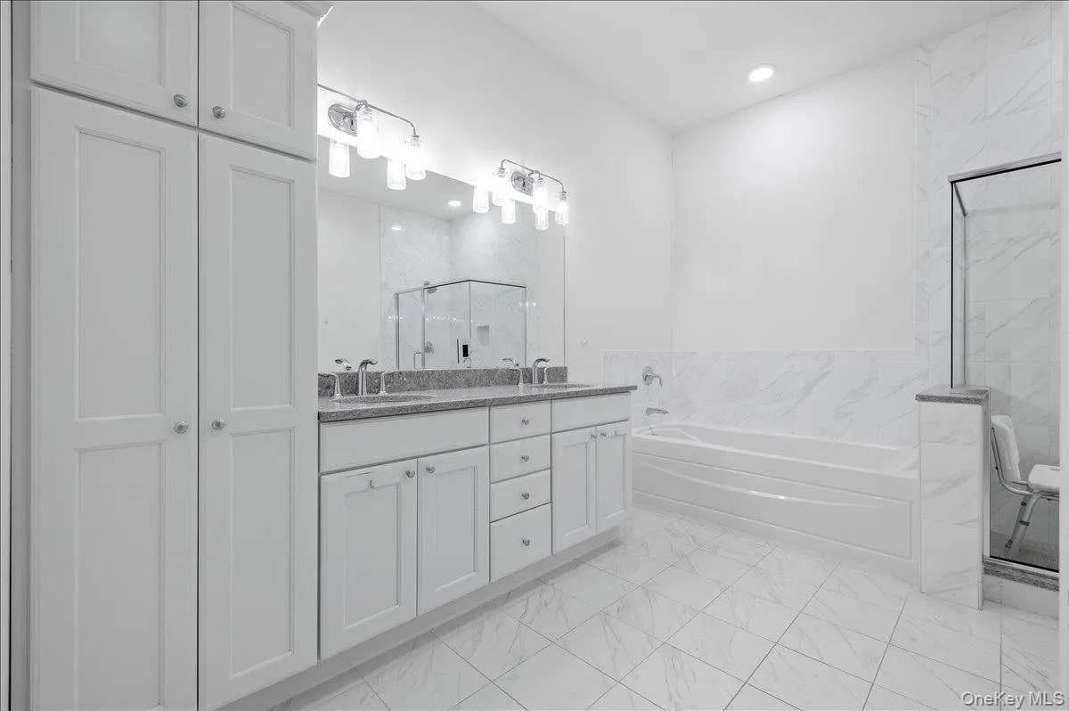 Full bathroom with double vanity, a marble finish shower, a bath, light marble finish floors, and recessed lighting Full bathroom with double vanity, a marble finish shower, a bath, light marble finish floors, and recessed lighting