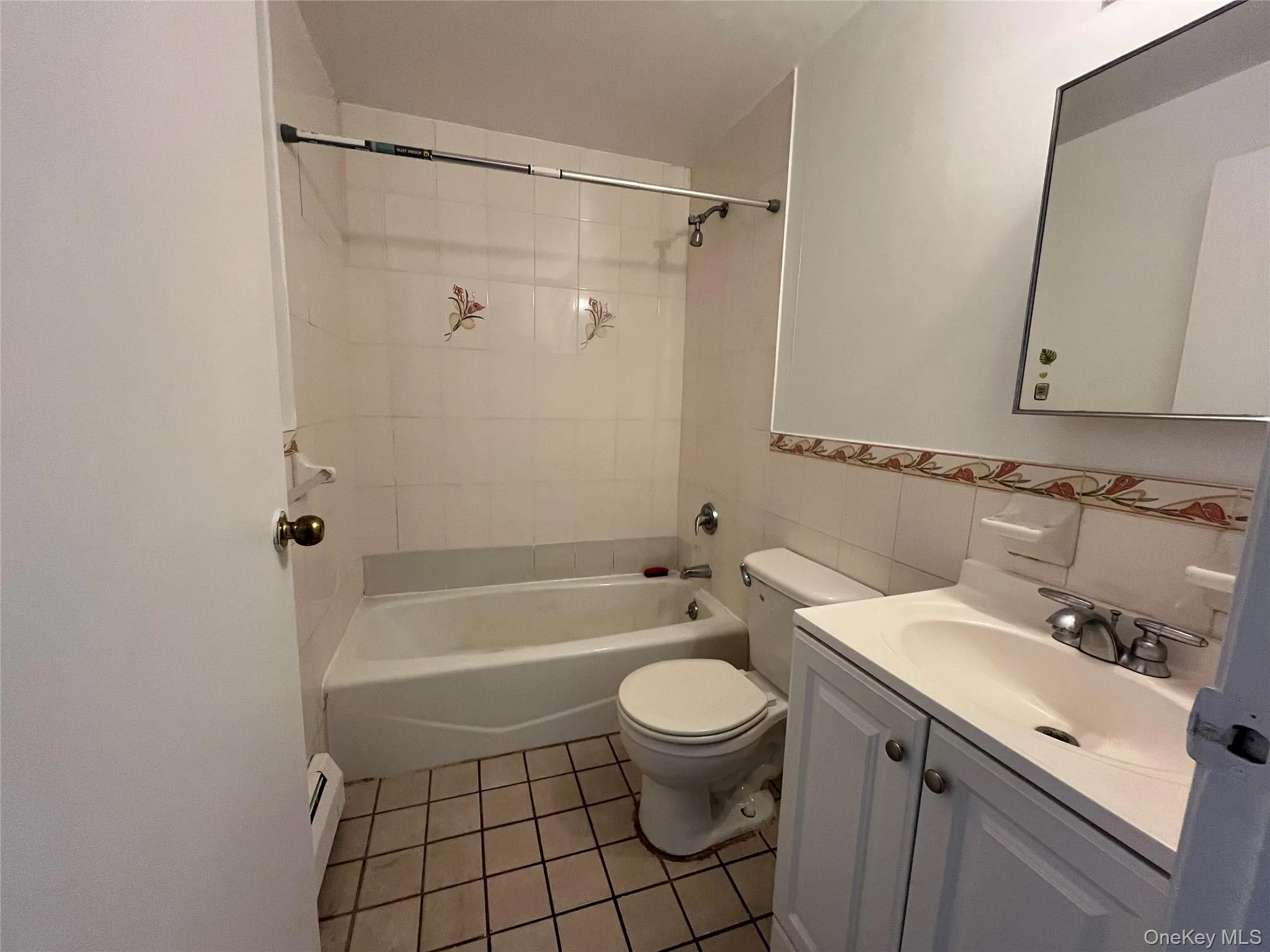 Bathroom featuring a white vanity with panel cabinetry and an integrated sink, a full-size bathtub with white subway tile surround, and neutral square floor tiles Bathroom featuring a white vanity with panel cabinetry and an integrated sink, a full-size bathtub with white subway tile surround, and neutral square floor tiles