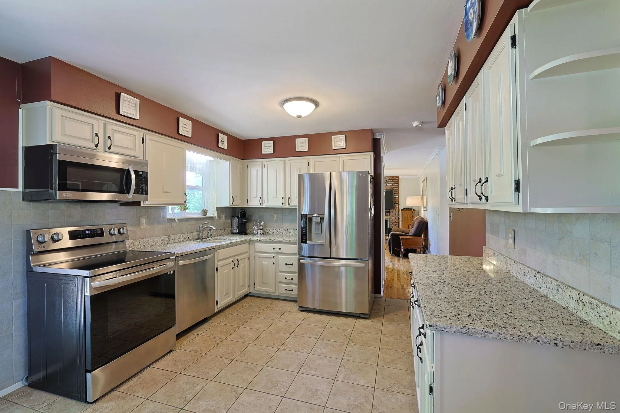 Kitchen featuring white cabinetry with dark hardware, stainless steel appliances, granite countertops, and a tiled backsplash Kitchen featuring white cabinetry with dark hardware, stainless steel appliances, granite countertops, and a tiled backsplash