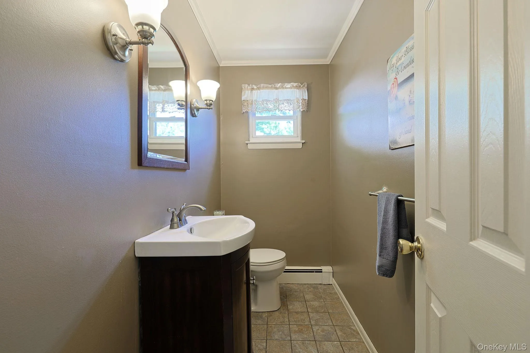 Compact bathroom featuring a dark wood-finish vanity with an integrated white sink, a coordinating wall-mounted mirror, and a vanity light fixture Compact bathroom featuring a dark wood-finish vanity with an integrated white sink, a coordinating wall-mounted mirror, and a vanity light fixture
