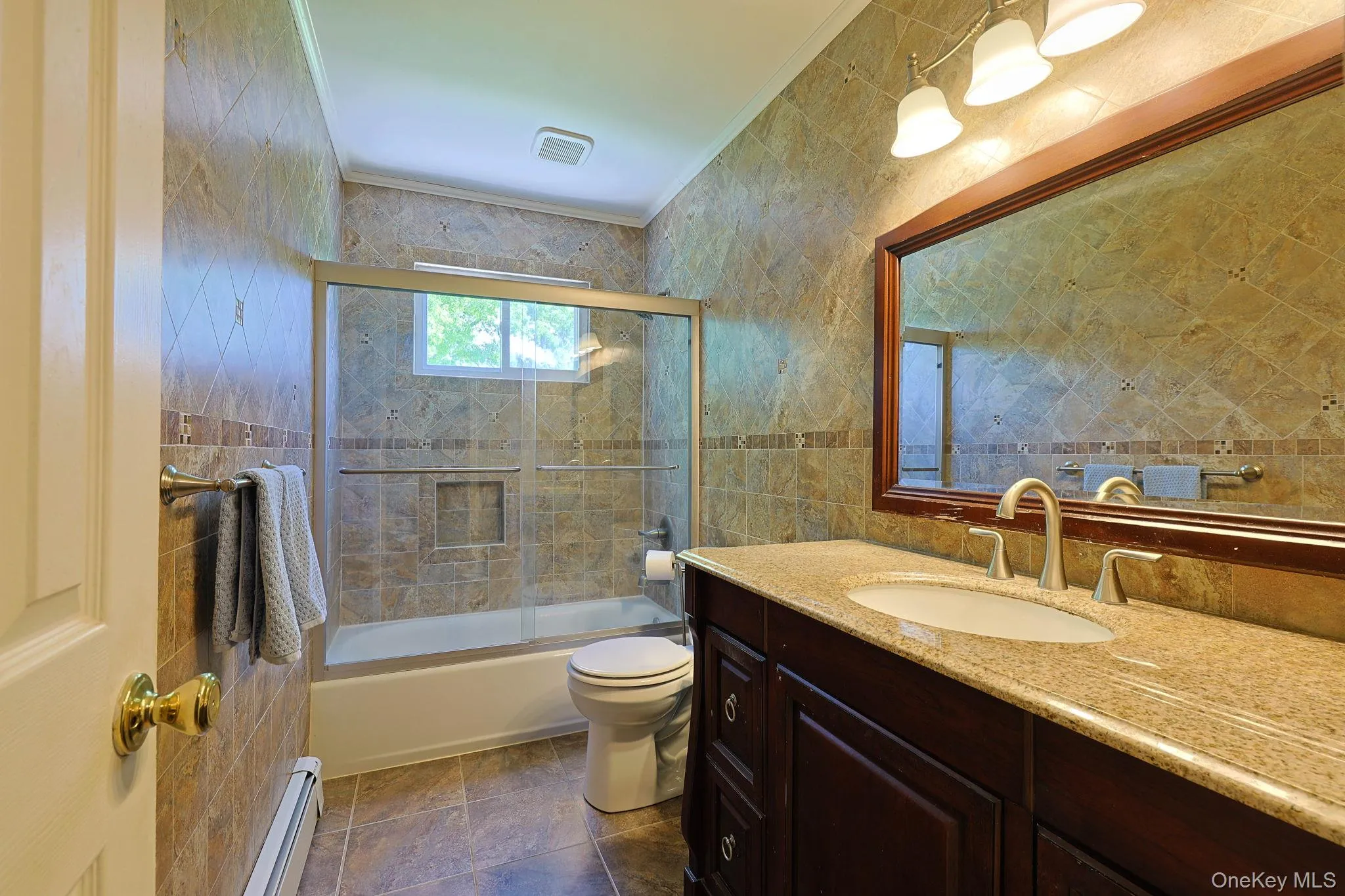 Bathroom featuring full-height tiled walls, a framed mirror, and a granite countertop with an undermount sink. Bathroom featuring full-height tiled walls, a framed mirror, and a granite countertop with an undermount sink.