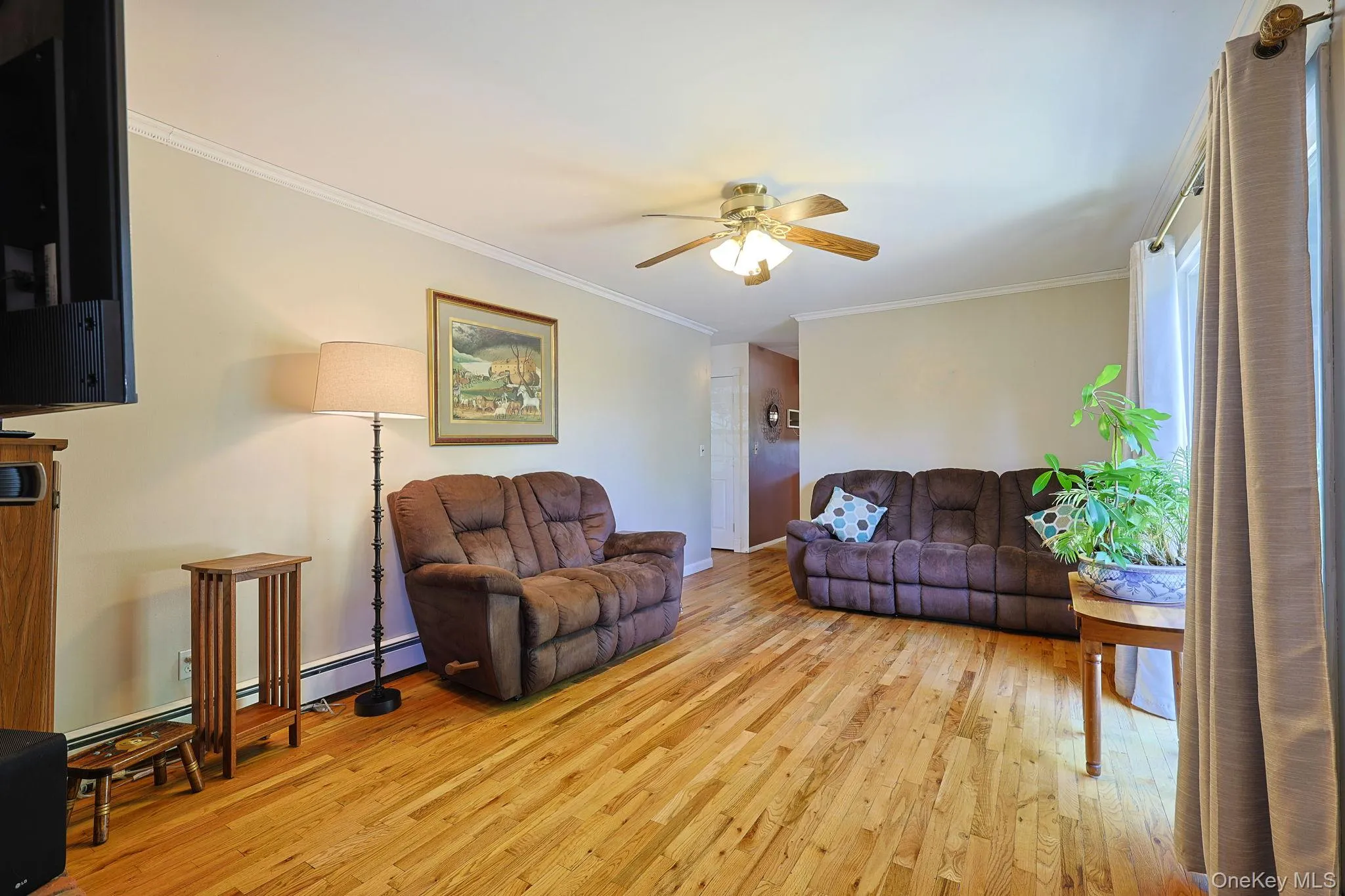 Bright living space featuring natural wood flooring, neutral wall tones, white crown molding, and a ceiling fan with light fixture Bright living space featuring natural wood flooring, neutral wall tones, white crown molding, and a ceiling fan with light fixture