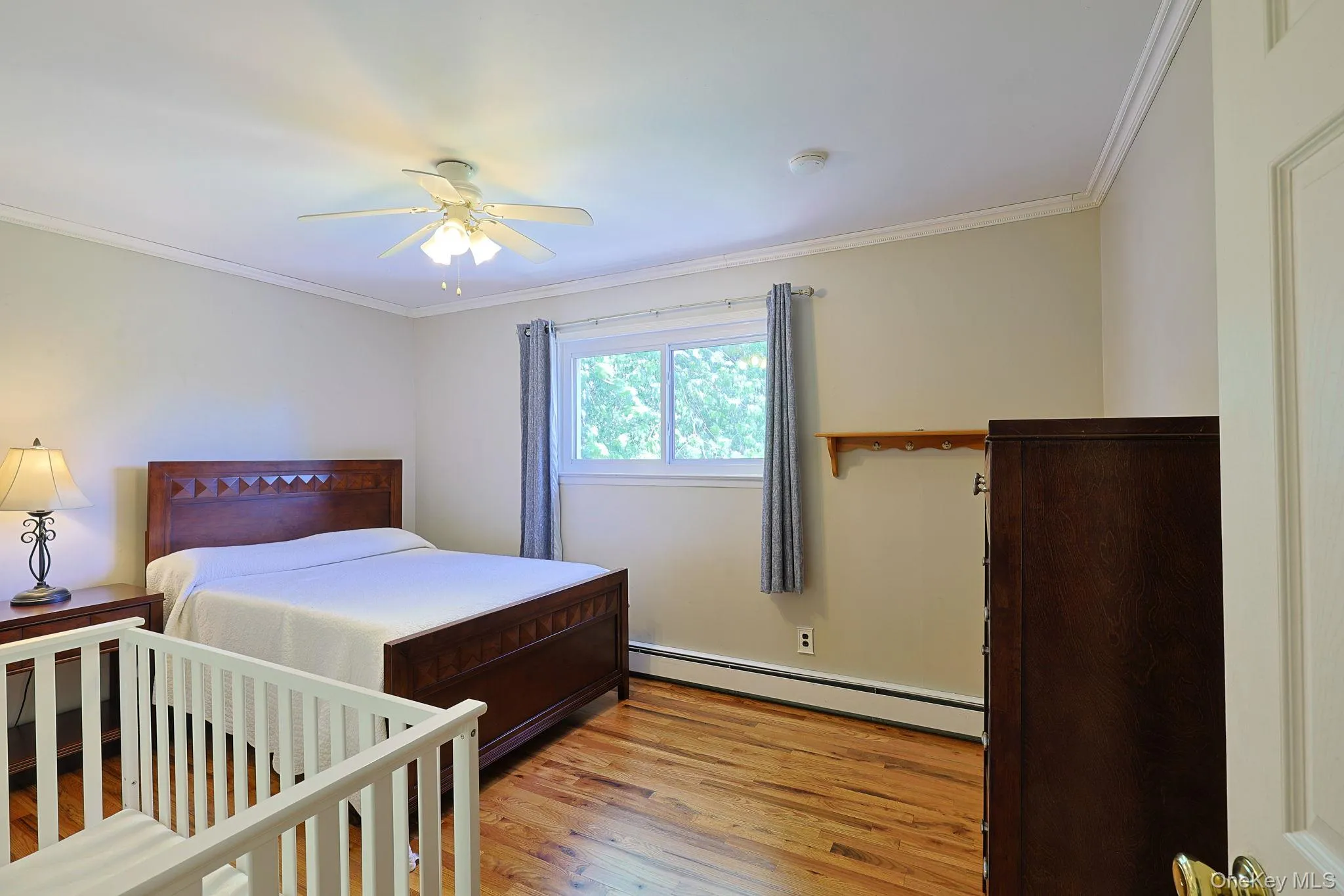 This bedroom features crown molding, a ceiling fan with integrated lighting, and a window for additional natural light. This bedroom features crown molding, a ceiling fan with integrated lighting, and a window for additional natural light.
