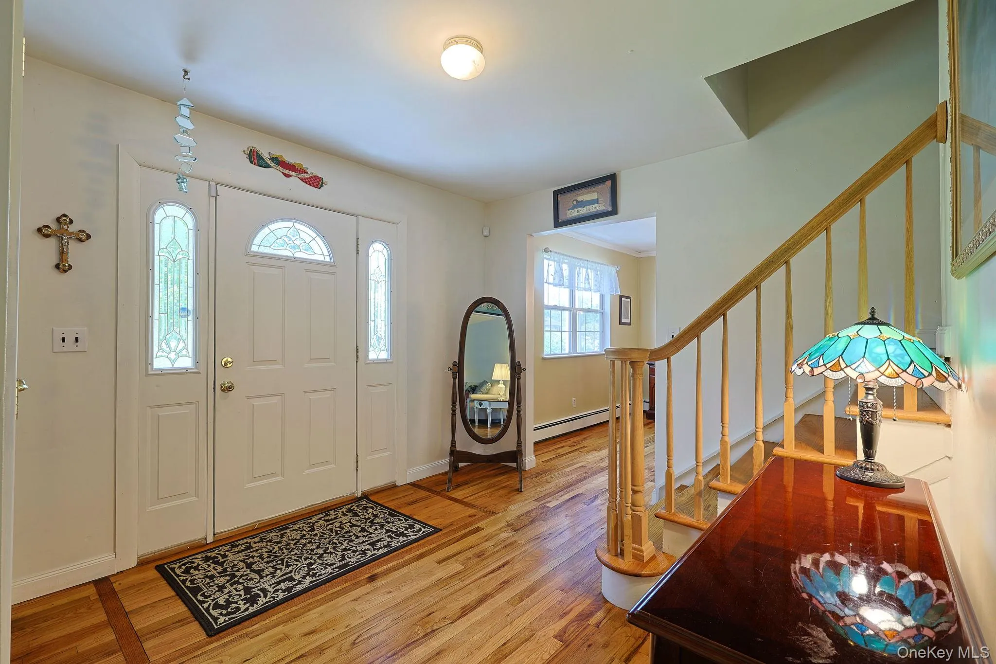 Entryway featuring wood-finish flooring, a white paneled entry door with an arched glass insert, and decorative glass panels. Entryway featuring wood-finish flooring, a white paneled entry door with an arched glass insert, and decorative glass panels.