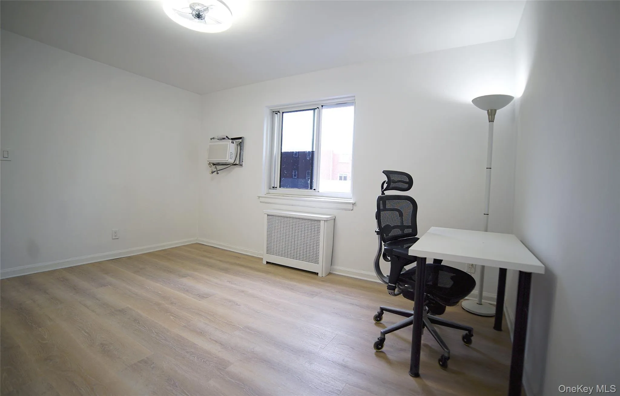 Office area with a wall mounted air conditioner, wood finished floors, baseboards, and radiator heating unit Office area with a wall mounted air conditioner, wood finished floors, baseboards, and radiator heating unit