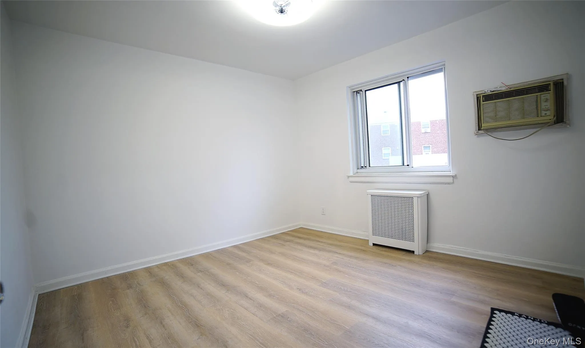 Unfurnished room with radiator, a wall mounted air conditioner, and wood finished floors Unfurnished room with radiator, a wall mounted air conditioner, and wood finished floors