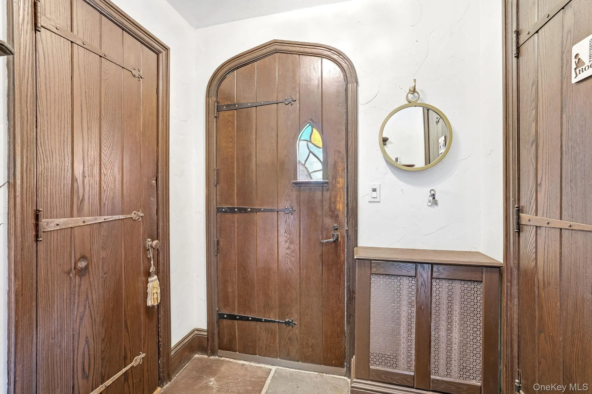 Arched wooden entry door with stained glass detail, complemented by dark wood paneling and stone tile flooring Arched wooden entry door with stained glass detail, complemented by dark wood paneling and stone tile flooring