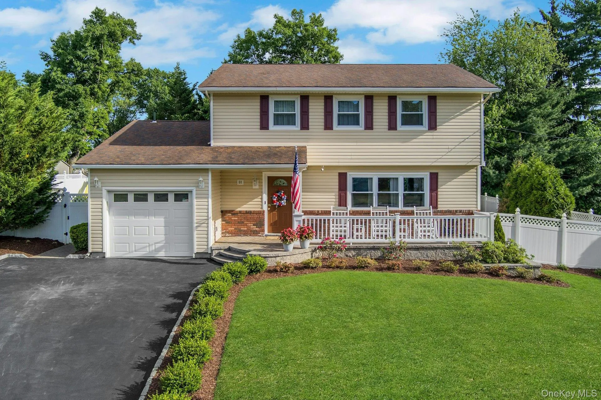 Two-story traditional residence featuring light yellow siding, a front porch with white railing, a dark asphalt driveway, an attached garage, and a lush green lawn Two-story traditional residence featuring light yellow siding, a front porch with white railing, a dark asphalt driveway, an attached garage, and a lush green lawn