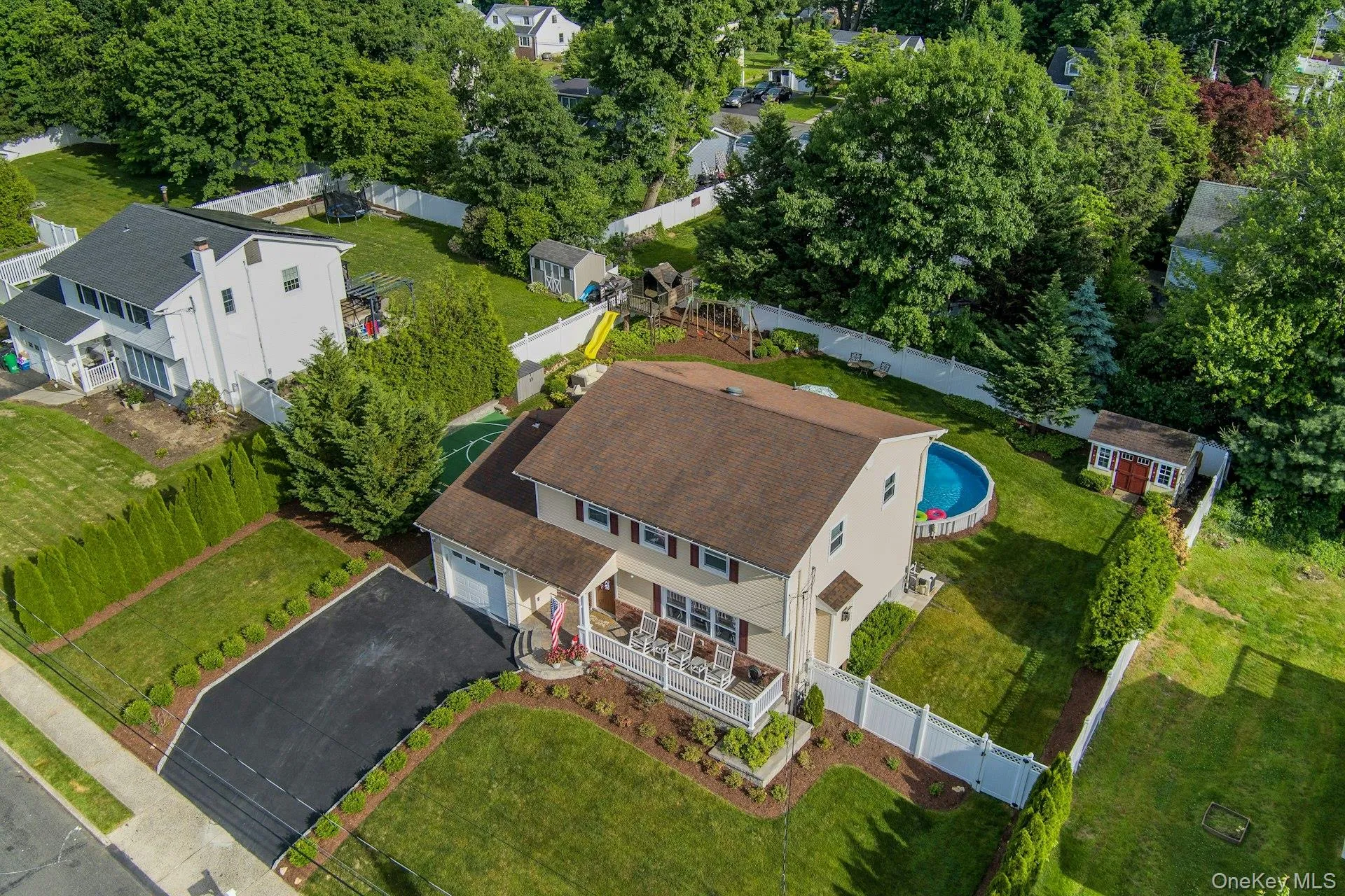Colonial featuring a front porch, an attached garage, a paved driveway, and a fenced backyard with an above-ground heated pool and a storage shed Colonial featuring a front porch, an attached garage, a paved driveway, and a fenced backyard with an above-ground heated pool and a storage shed