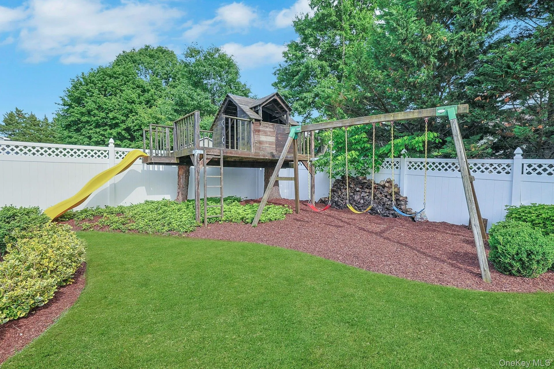 Expansive backyard featuring a manicured lawn, a wooden playset with a slide and swings, and a white lattice-top fence Expansive backyard featuring a manicured lawn, a wooden playset with a slide and swings, and a white lattice-top fence