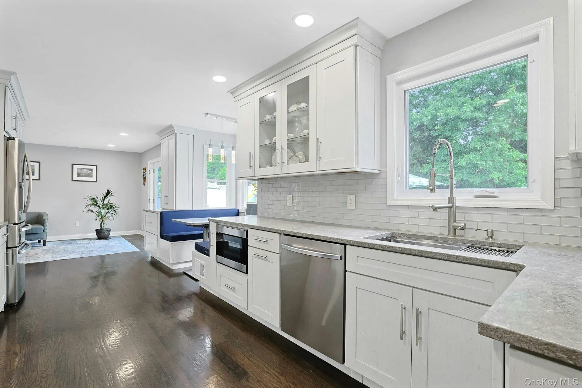 Modern kitchen featuring dark wood-finish flooring, white shaker cabinetry, stainless steel appliances, and light-toned countertops Modern kitchen featuring dark wood-finish flooring, white shaker cabinetry, stainless steel appliances, and light-toned countertops