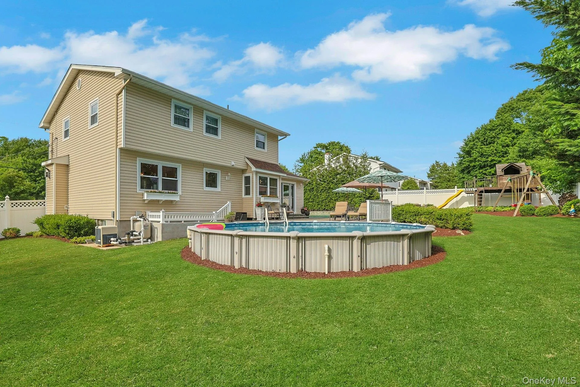Expansive rear yard featuring an above-ground heated pool, a swing set with slide, and a beige vinyl-sided exterior Expansive rear yard featuring an above-ground heated pool, a swing set with slide, and a beige vinyl-sided exterior