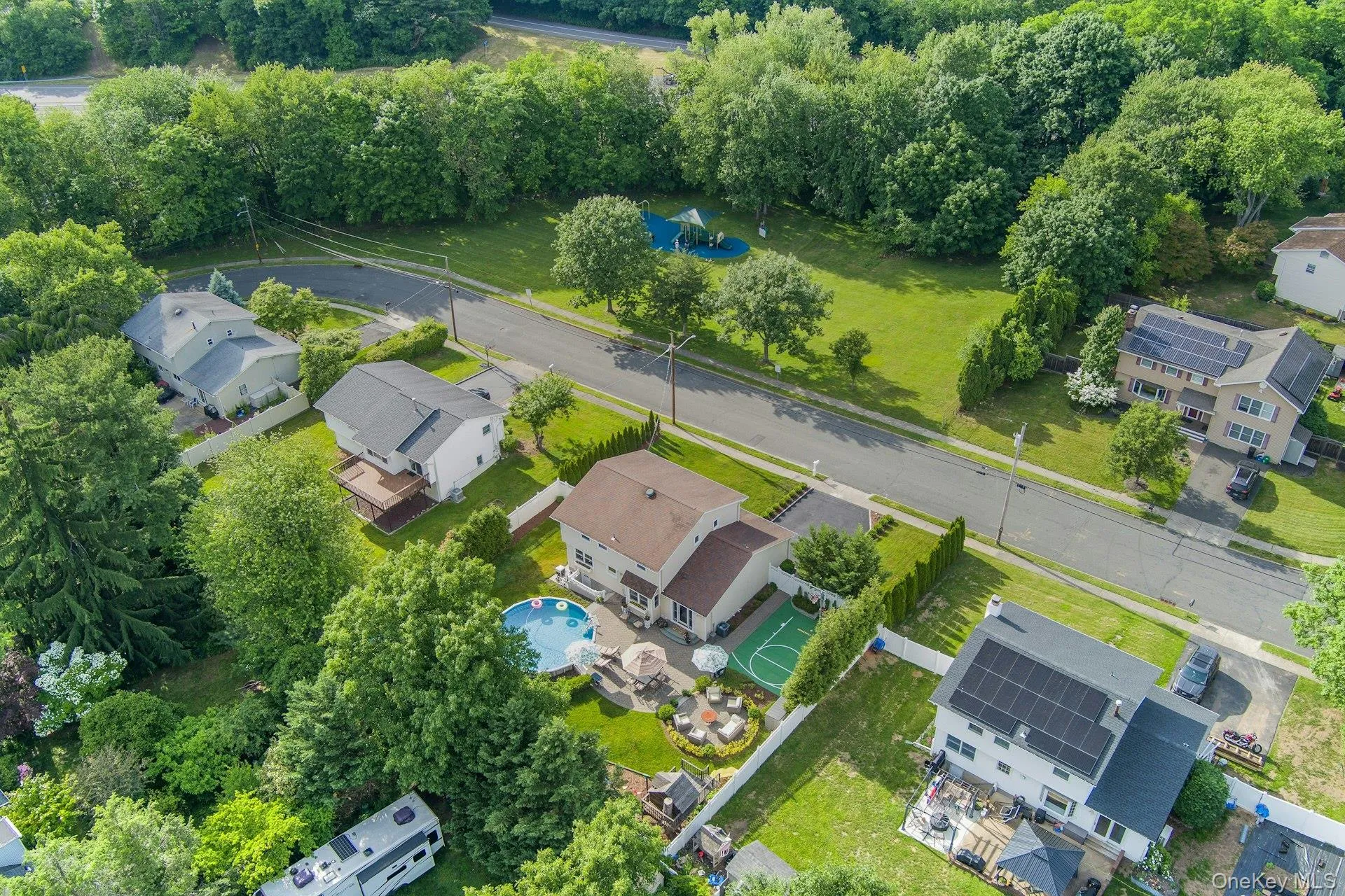 Aerial view highlighting a residential property featuring a backyard heated swimming pool, a dedicated sports court, a paved patio area with outdoor seating, and mature trees providing natural screening Aerial view highlighting a residential property featuring a backyard heated swimming pool, a dedicated sports court, a paved patio area with outdoor seating, and mature trees providing natural screening