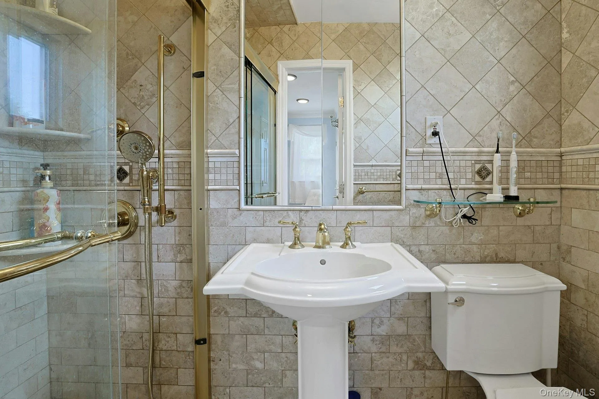 Bathroom featuring a pedestal sink, gold-finish fixtures, and a glass-enclosed shower with a handheld showerhead Bathroom featuring a pedestal sink, gold-finish fixtures, and a glass-enclosed shower with a handheld showerhead