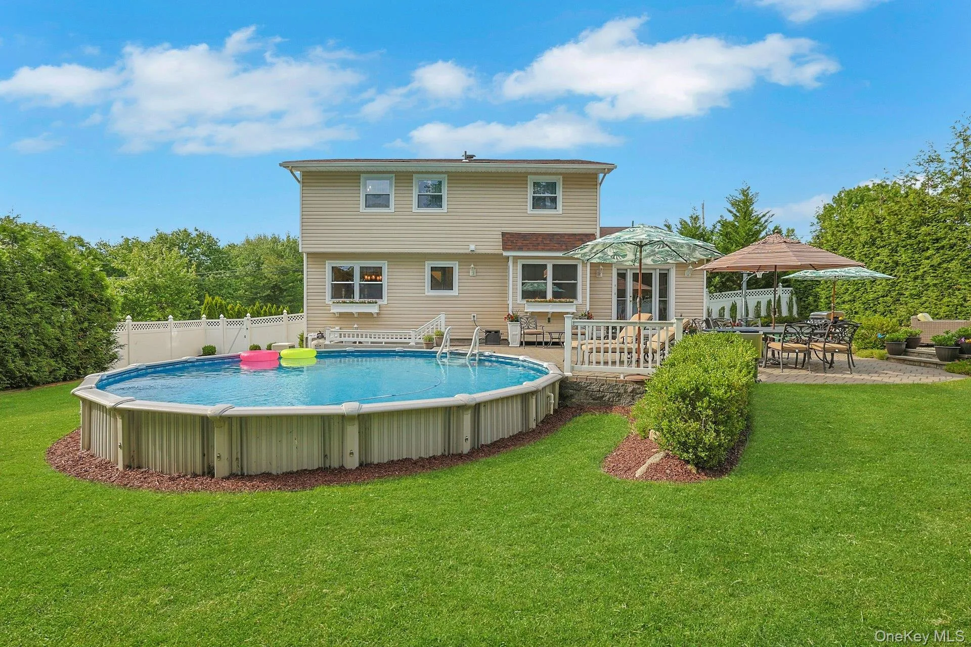 Rear exterior featuring an above-ground heated pool, a multi-level deck, and a stone paver patio Rear exterior featuring an above-ground heated pool, a multi-level deck, and a stone paver patio