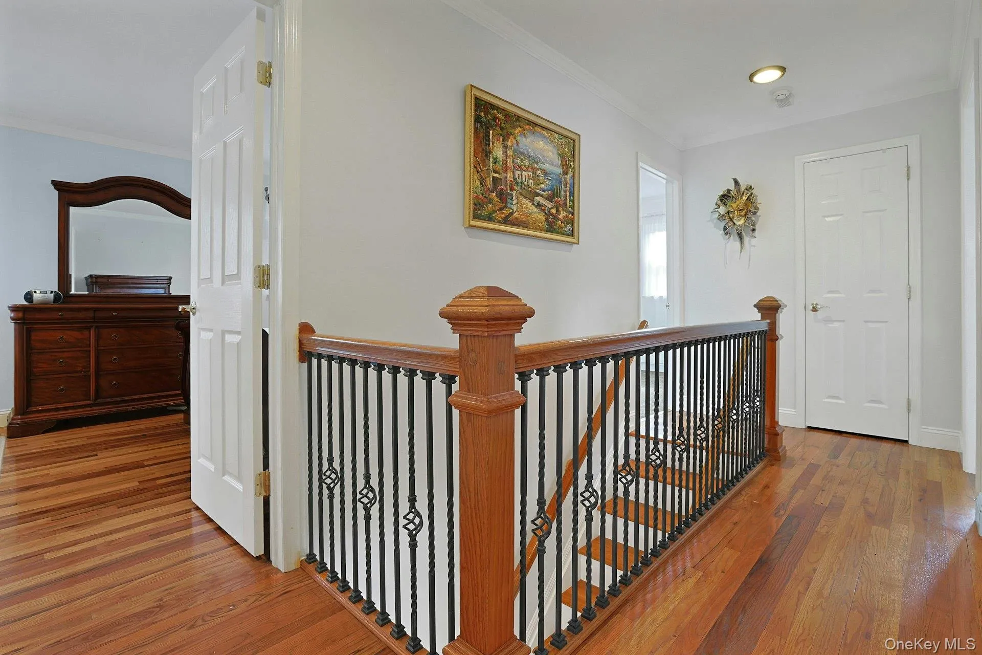 Hardwood flooring extends throughout this upper-level landing, featuring a staircase with wood newel posts and handrail, and black wrought iron balusters Hardwood flooring extends throughout this upper-level landing, featuring a staircase with wood newel posts and handrail, and black wrought iron balusters