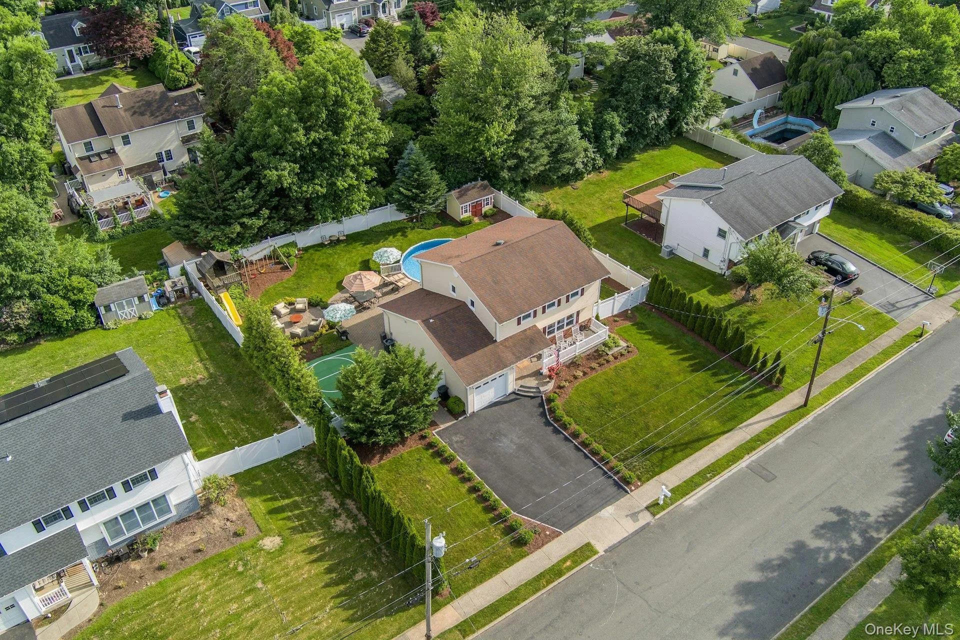 Colonial featuring a paved driveway, front lawn, and mature landscaping Colonial featuring a paved driveway, front lawn, and mature landscaping