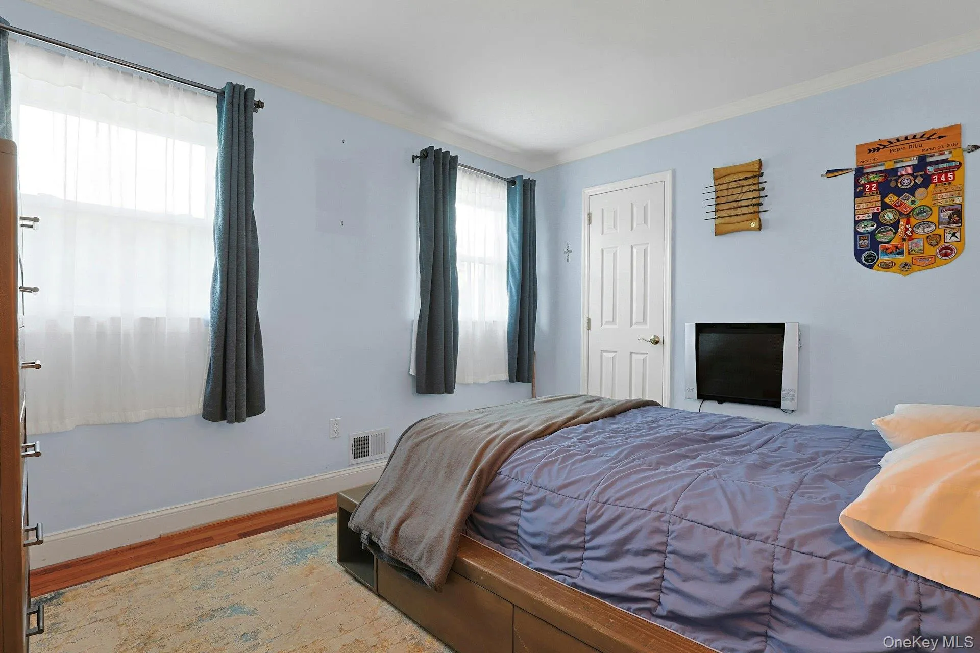 Bedroom featuring wood-finish flooring, light blue wall paint, white baseboards, crown molding, and a white paneled door Bedroom featuring wood-finish flooring, light blue wall paint, white baseboards, crown molding, and a white paneled door