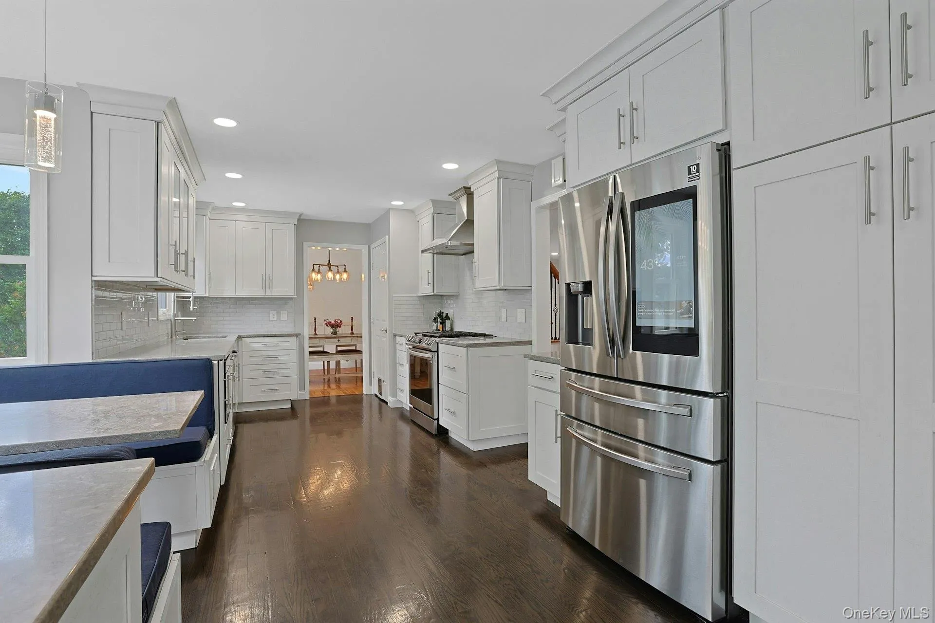 Kitchen featuring white shaker cabinetry, stainless steel appliances, dark wood-finish flooring, and light-toned countertops Kitchen featuring white shaker cabinetry, stainless steel appliances, dark wood-finish flooring, and light-toned countertops