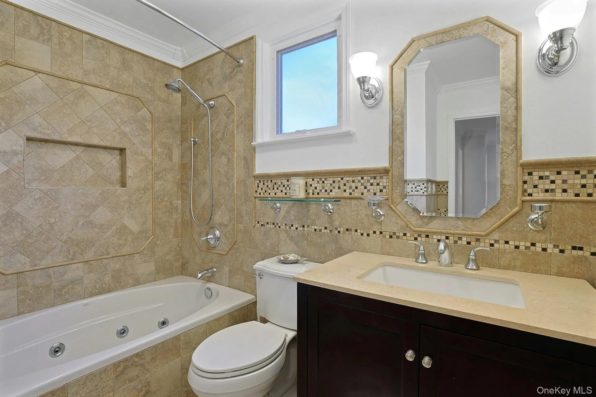 Bathroom featuring a jetted tub, tiled shower surround with niche, dark wood vanity with an integrated sink, mosaic tile accents, and a framed mirror Bathroom featuring a jetted tub, tiled shower surround with niche, dark wood vanity with an integrated sink, mosaic tile accents, and a framed mirror