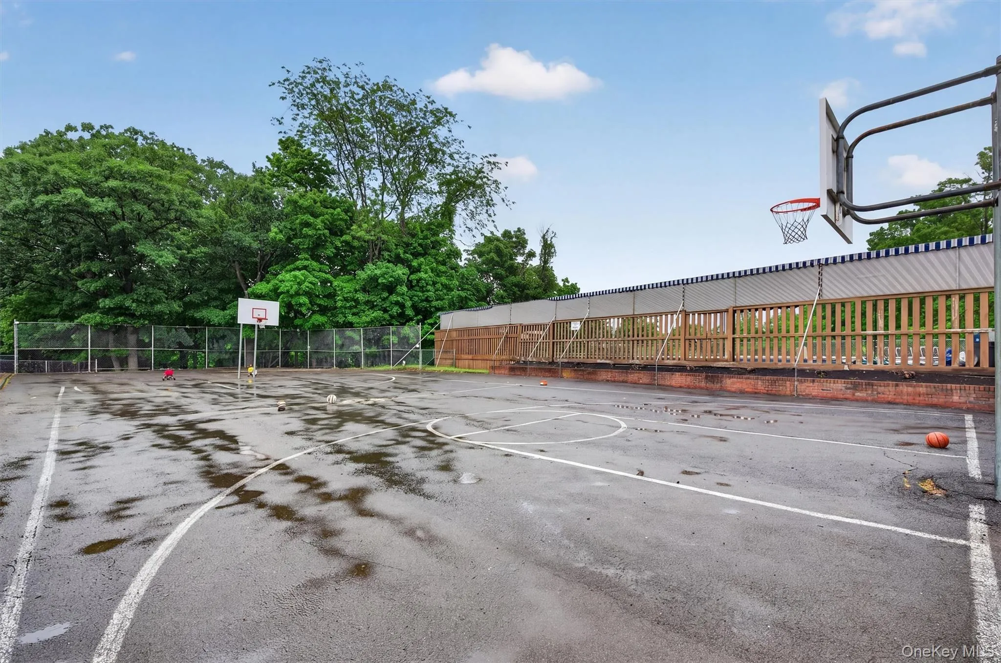Outdoor basketball court with two hoops, surrounded by a chain-link fence and a wooden fence Outdoor basketball court with two hoops, surrounded by a chain-link fence and a wooden fence